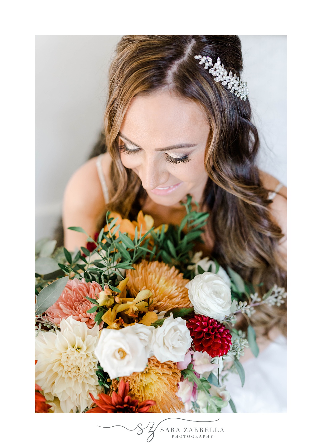bride smiles down at fall bouquet with red, white, and orange flowers