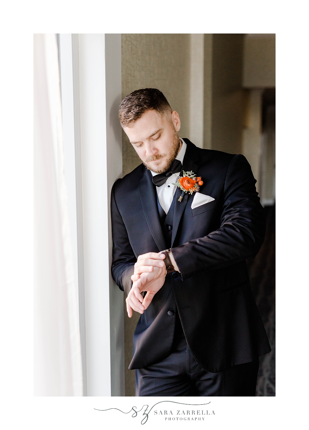 groom looks down at watch while leaning against wall at Newport Harbor Island Resort