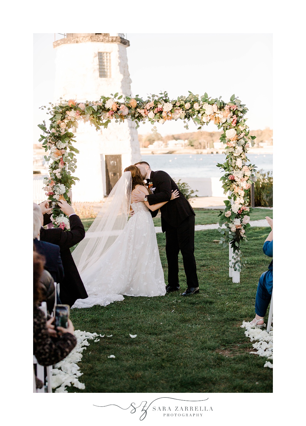 bride and groom kiss under fall arbor with flowers