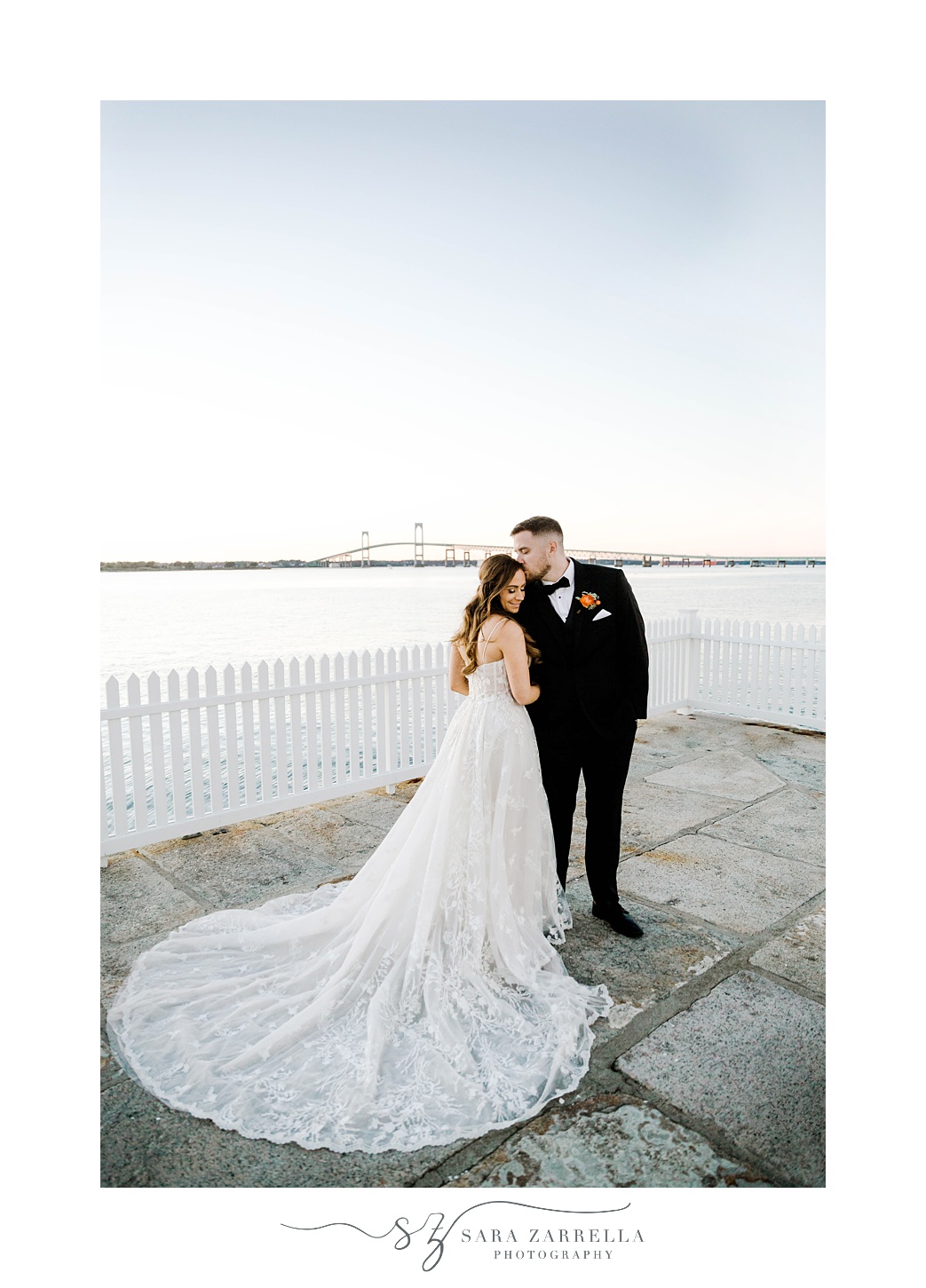 groom kisses bride's forehead by white picket fence outside Newport Harbor Island Resort