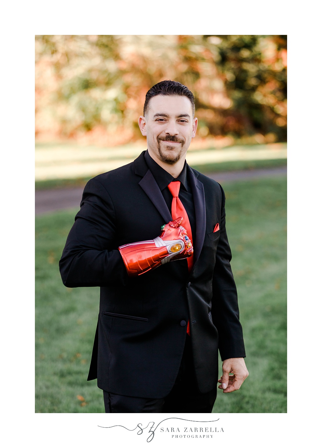 groom stands with Iron Man arm during portraits at Quidnessett Country Club