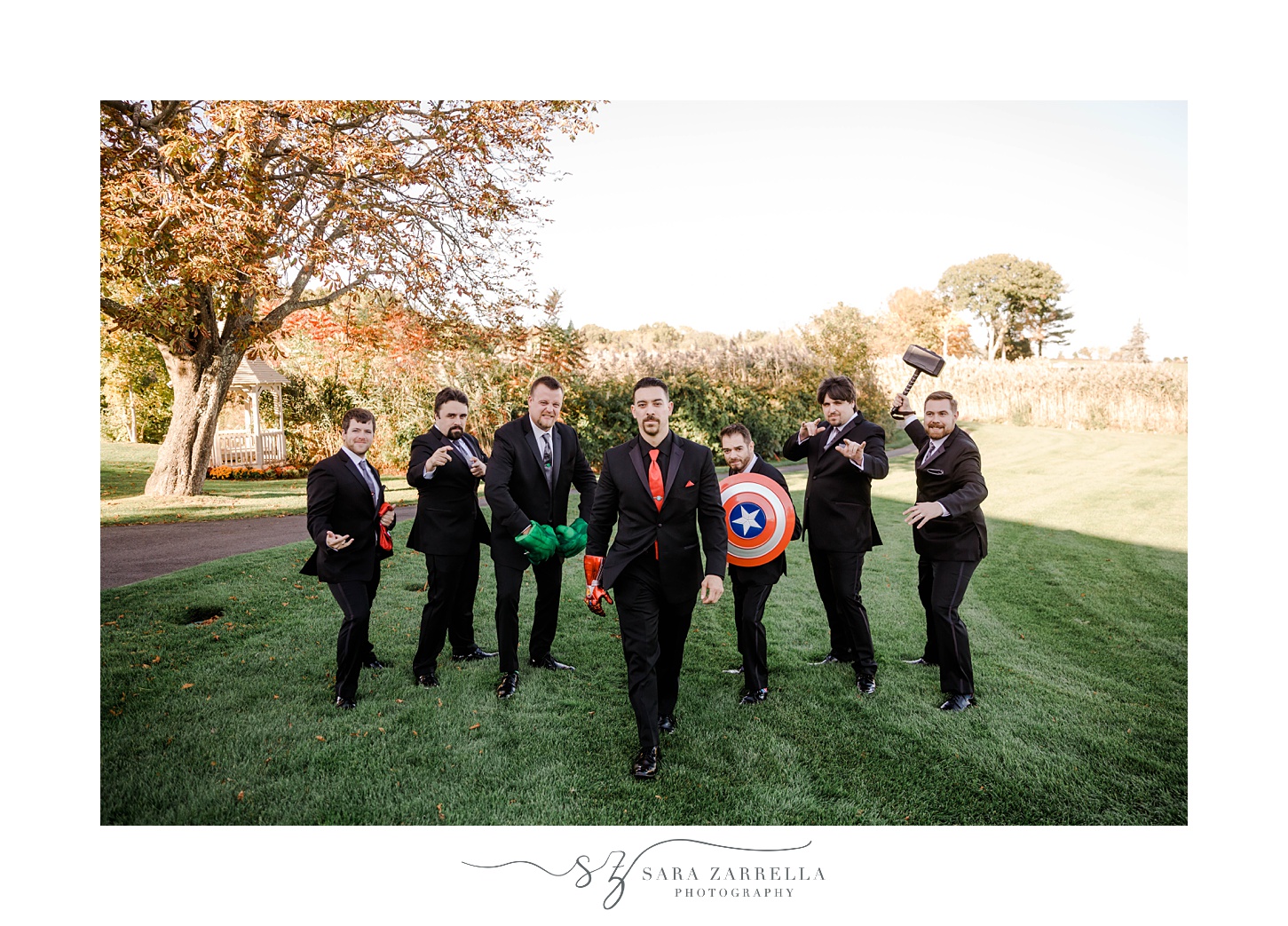 groom and groomsmen walk with Marvel character props on lawn at Quidnessett Country Club