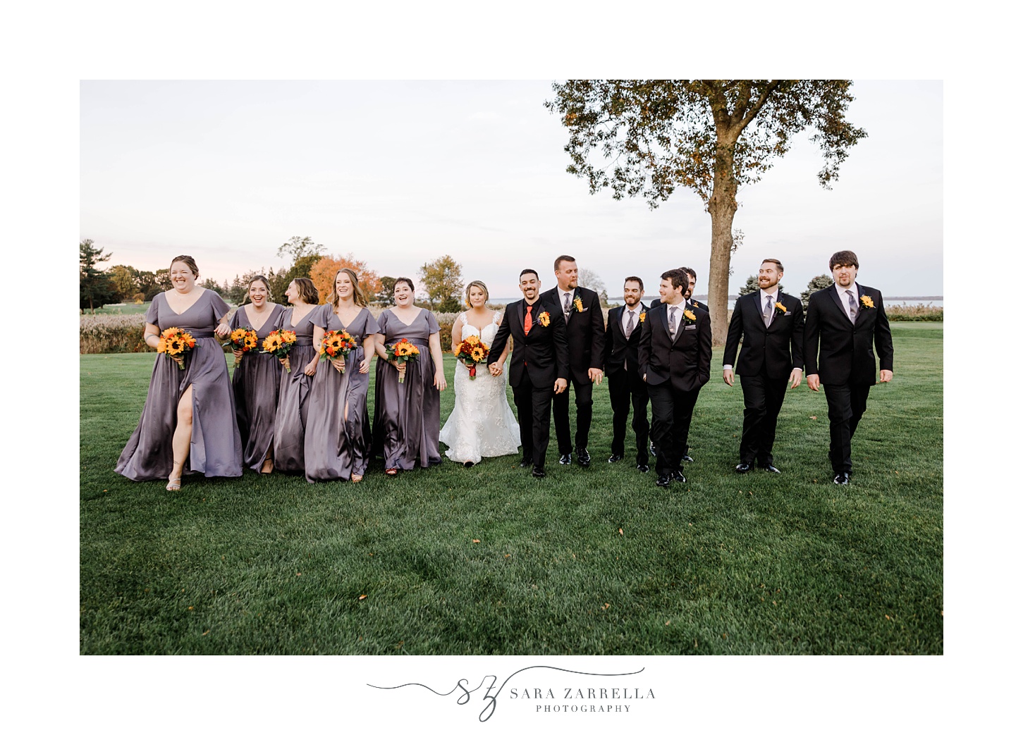 newlyweds walk with wedding party in black and mauve on lawn at Quidnessett Country Club