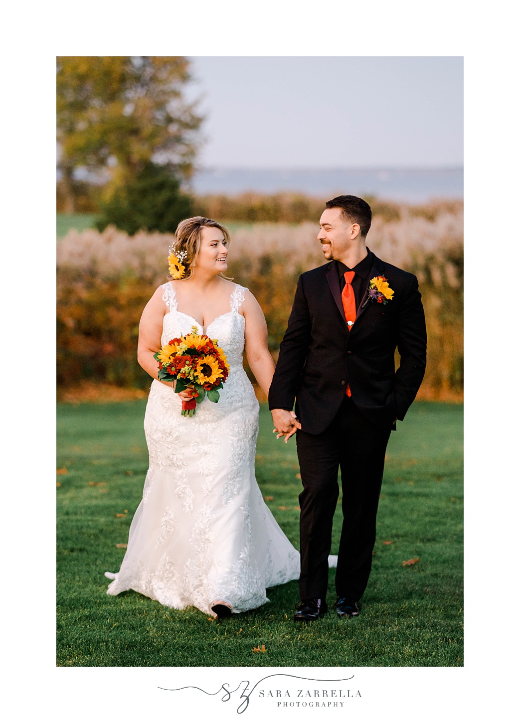 bride and groom hold hands walking across lawn while bride holds sunflower bouquet 