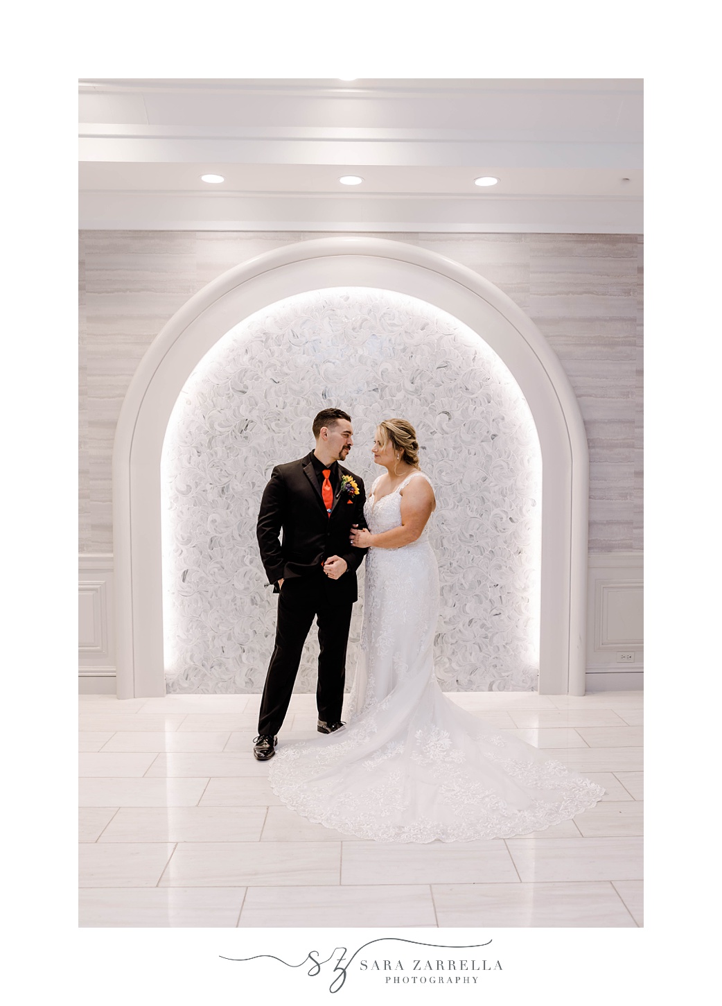 bride and groom hug in white archway inside Quidnessett Country Club