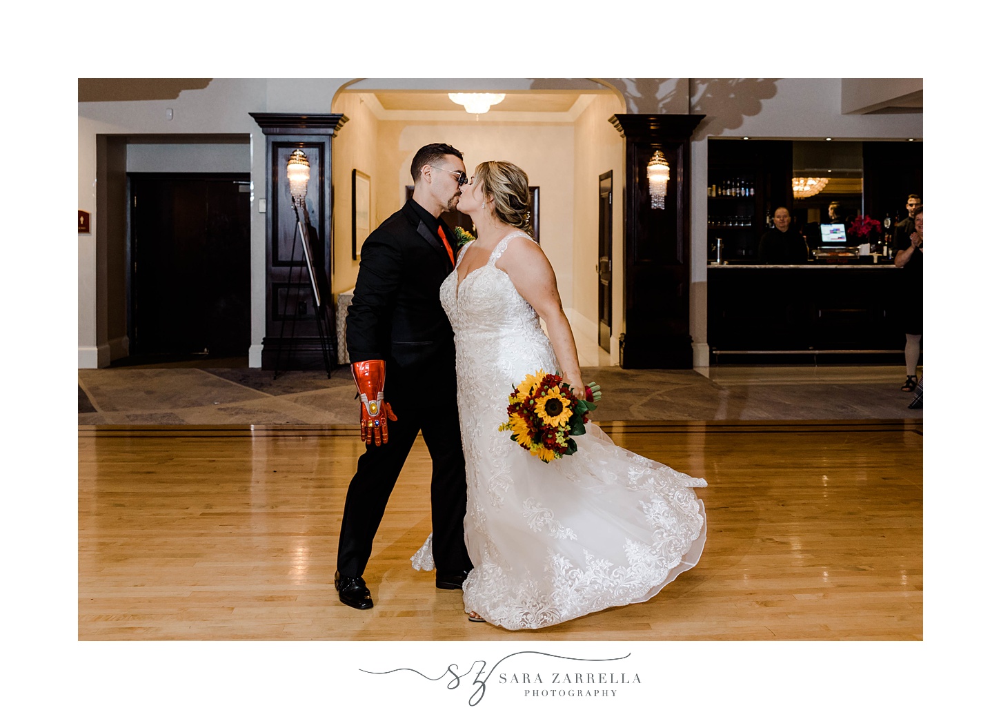 newlyweds kiss on dance floor while bride holds bouquet of sunflowers and groom wears Iron Man prop arm