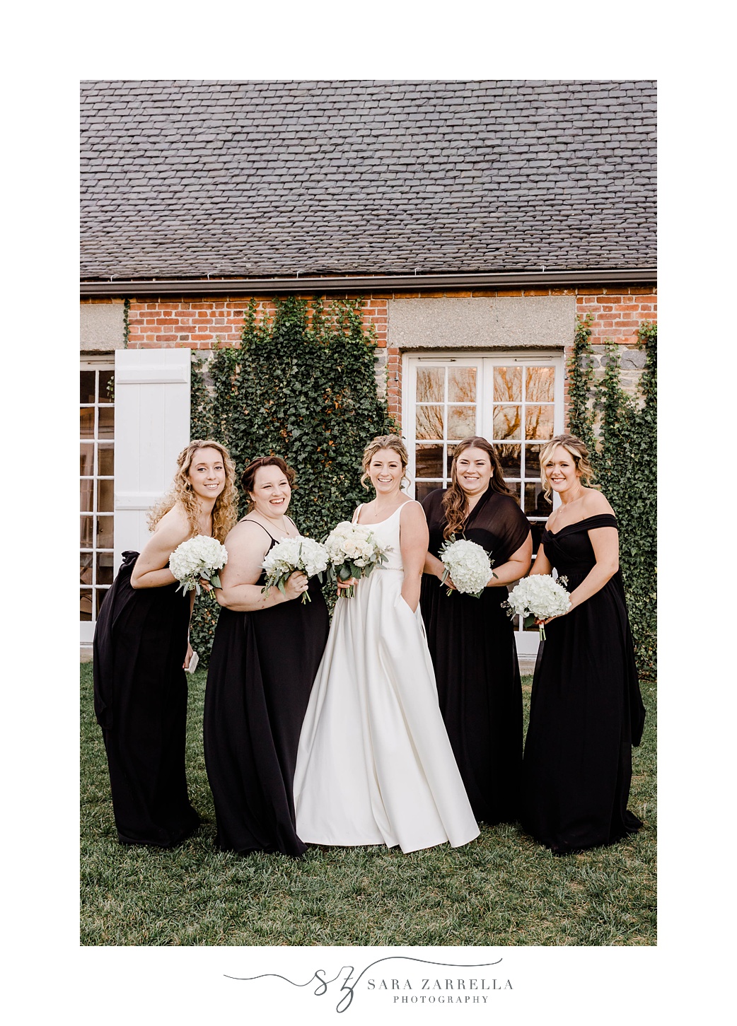 bride poses with bridesmaids in black gowns with white bouquets 