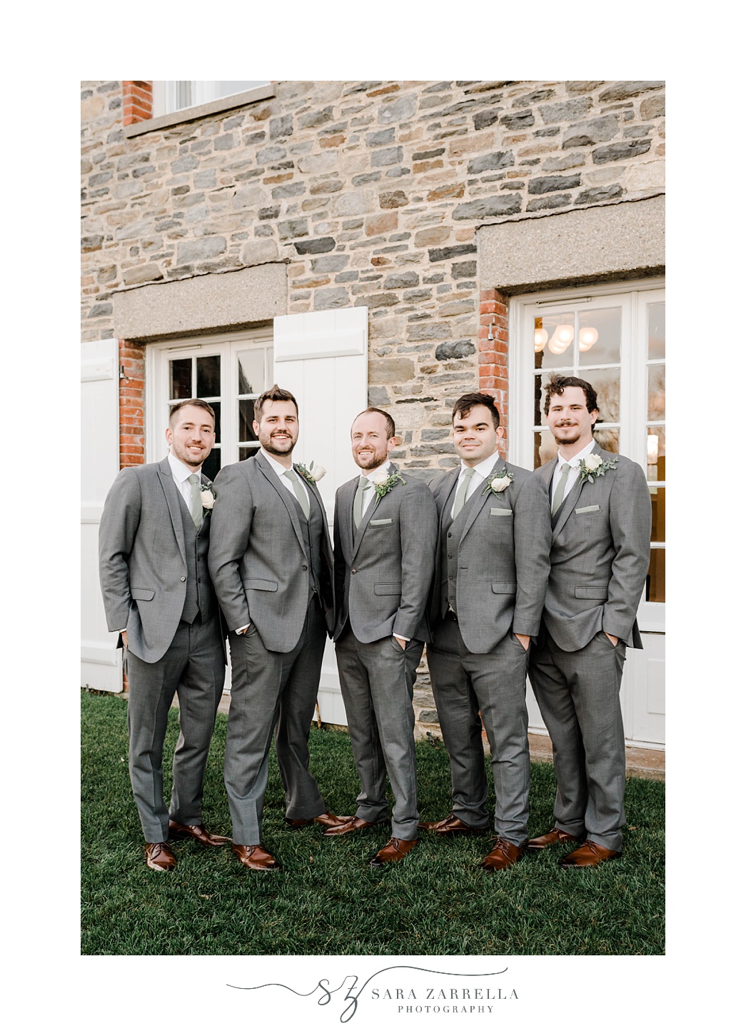 groom and groomsmen pose in grey suits with hands in pockets