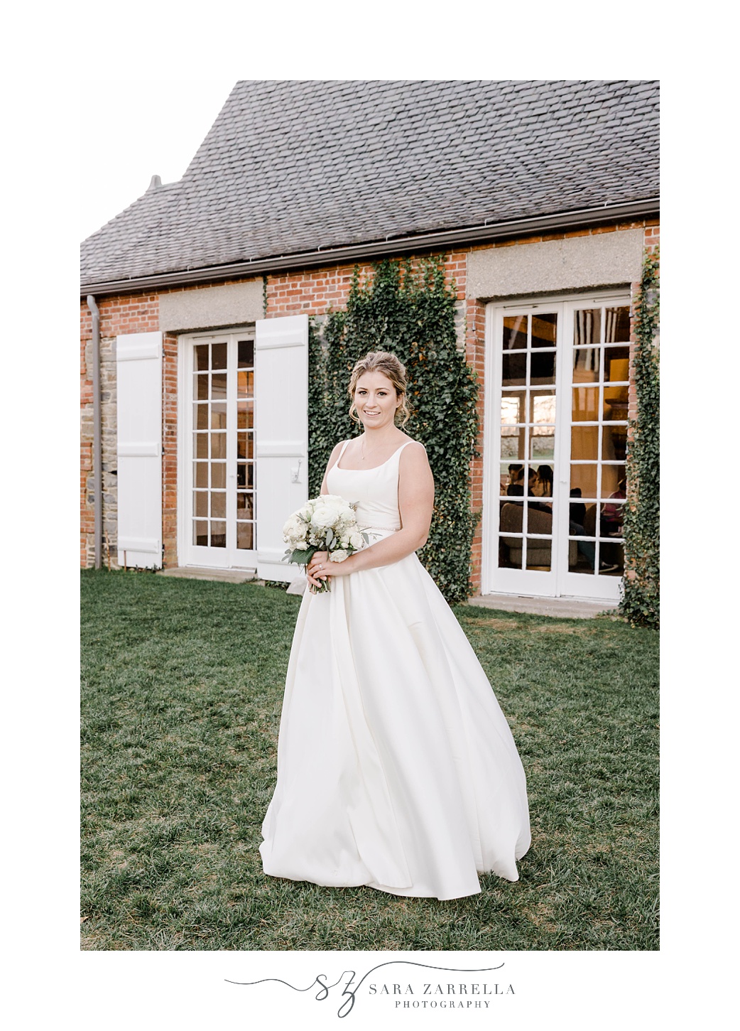 bride stands with bouquet of white flowers outside brick building at Shepard's Run