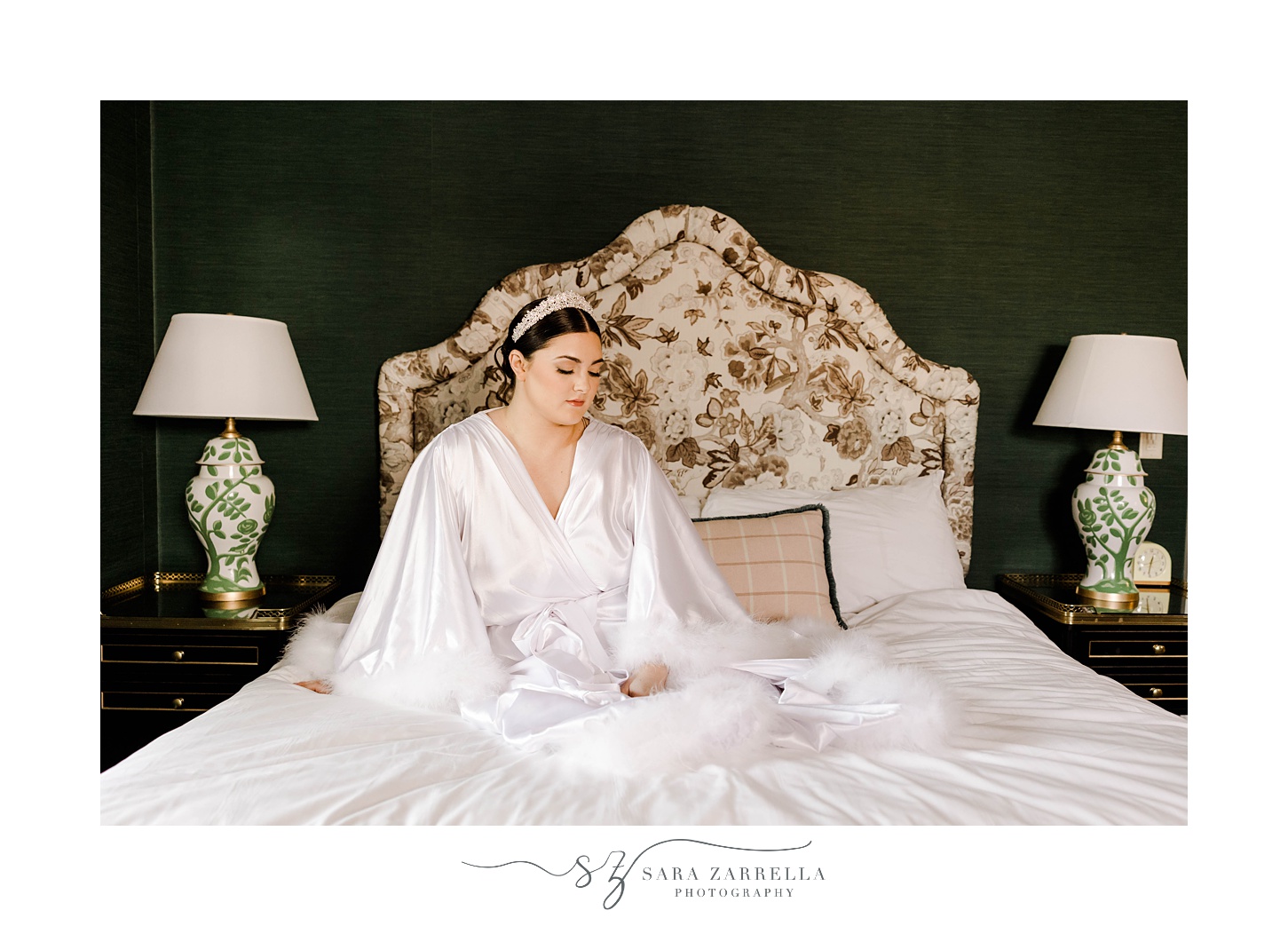 bride sits on bed at The Graduate Providence in ivory robe with white headband 