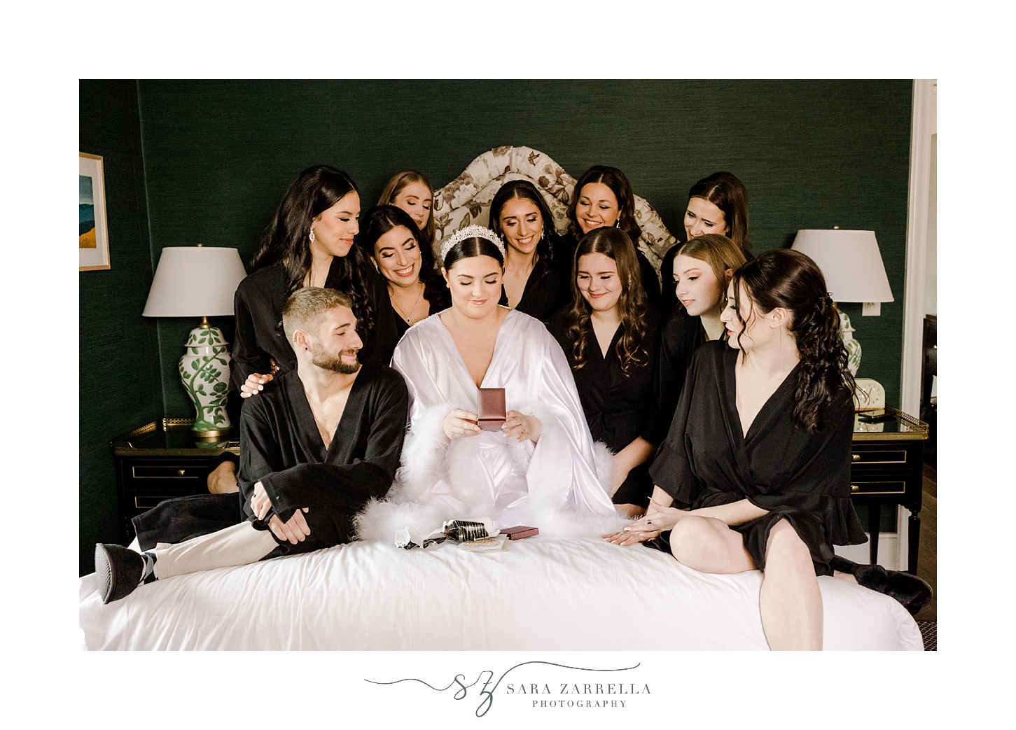 bride sits on bed reading a letter with bridal party around her in black robes 
