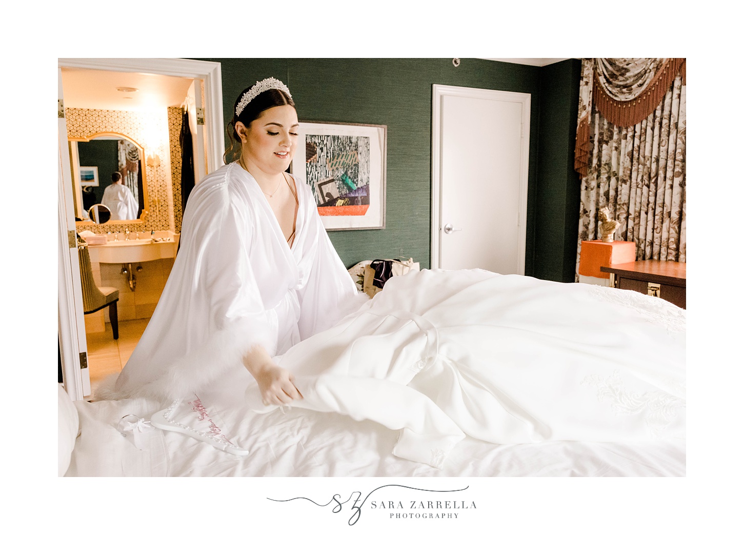 bride adjusts skirt of wedding gown on bed 