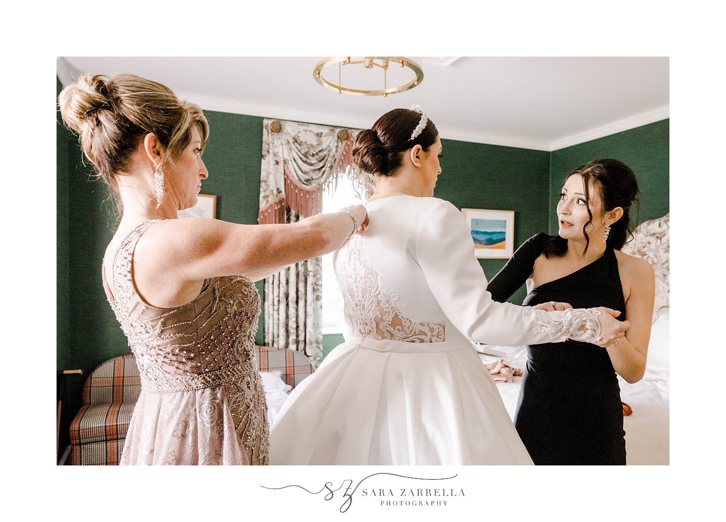 bridesmaid in black gown looks at bride laughing during prep 
