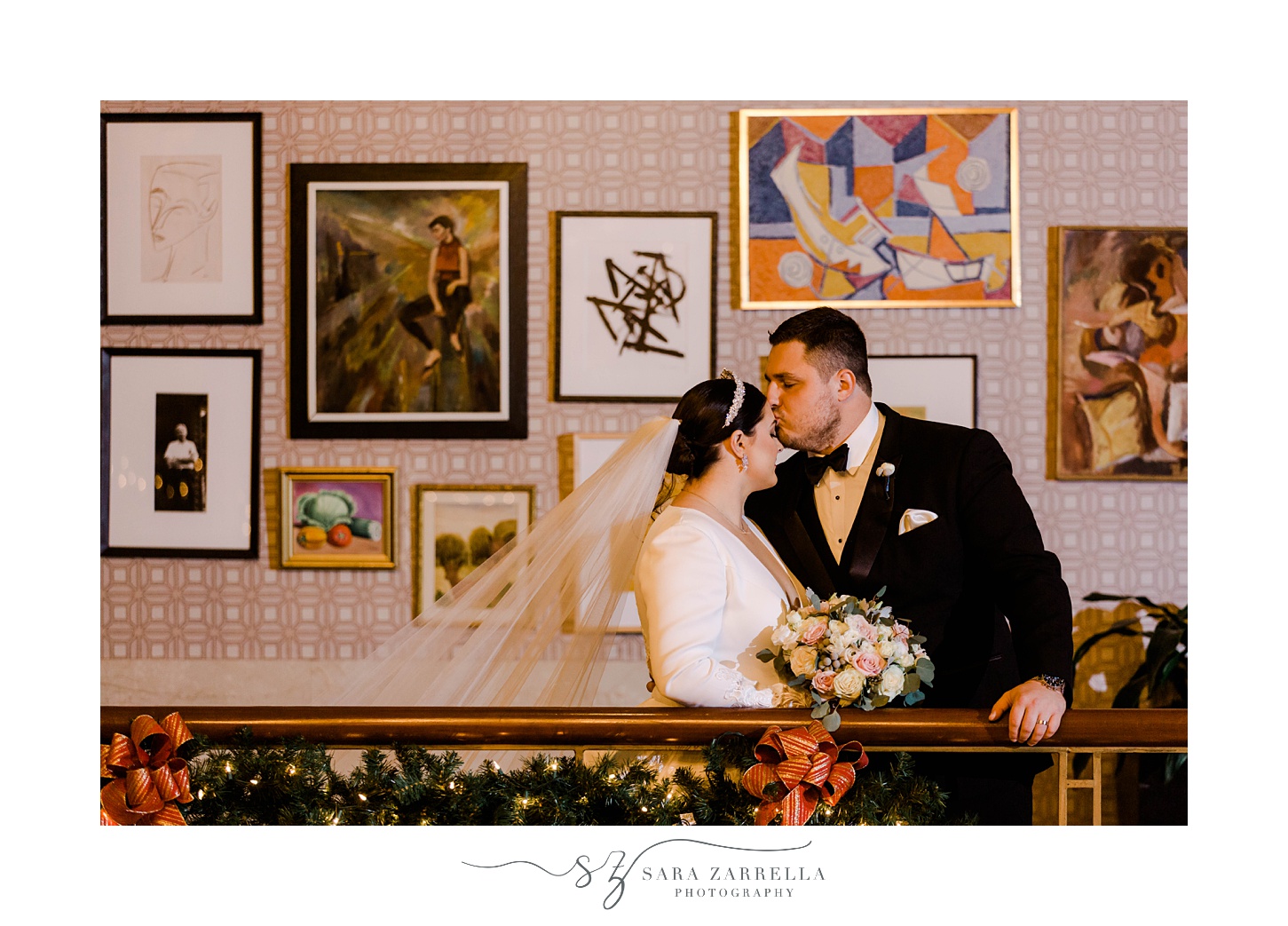 groom kisses bride's forehead in front of art display 