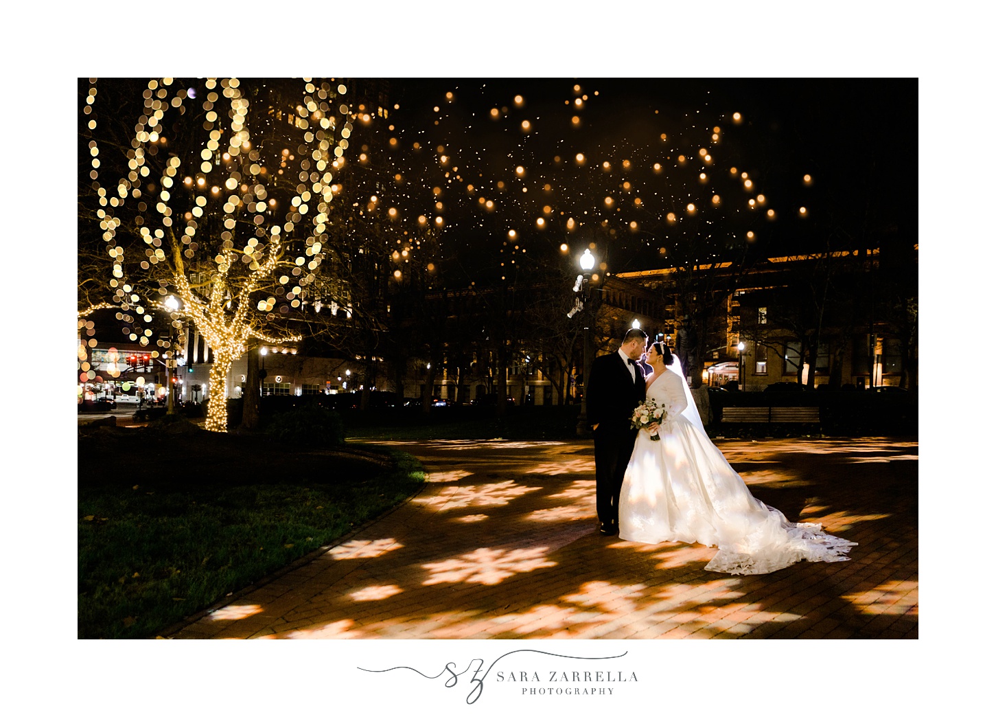 newlyweds hug in park in Providence RI at night with Christmas lights around them 