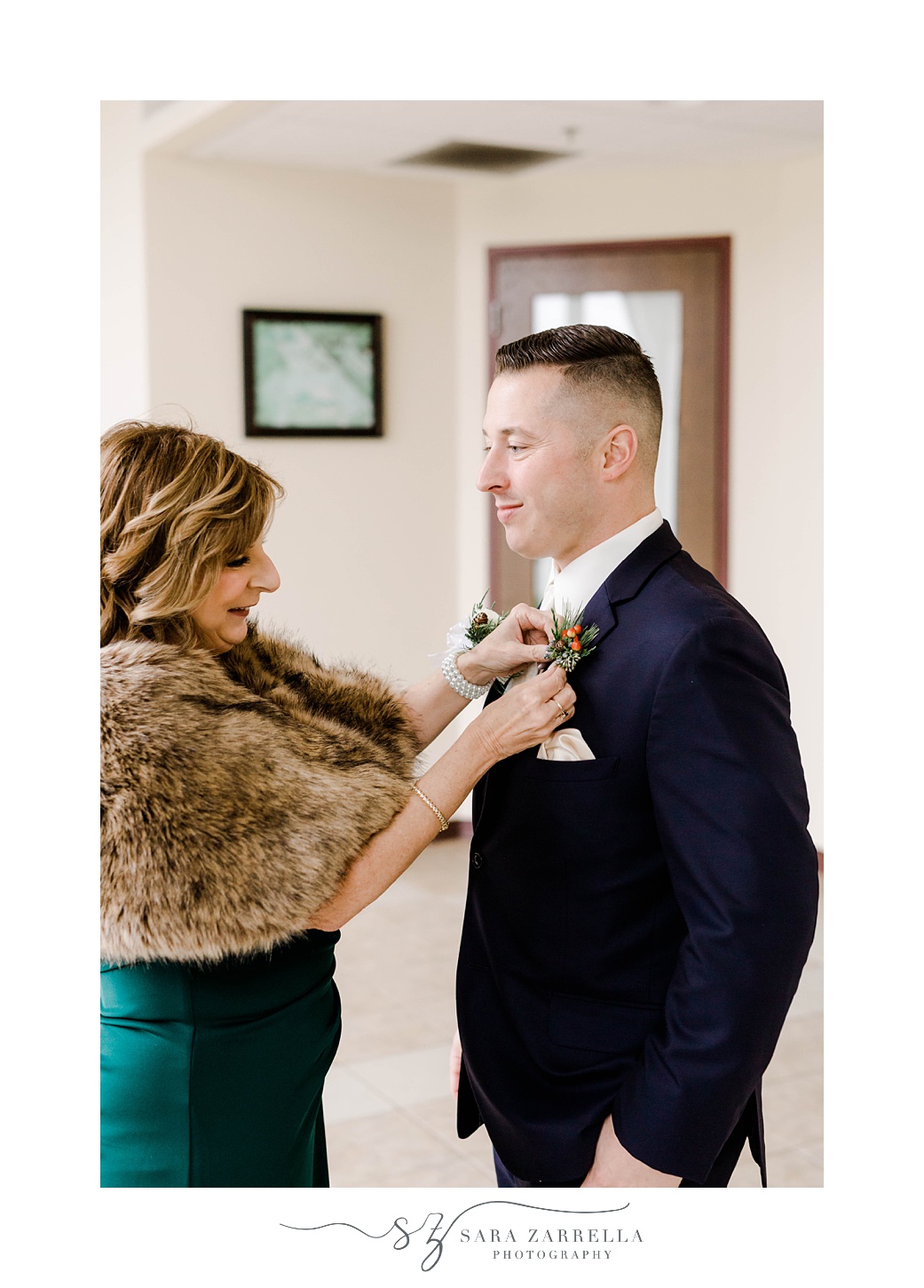mother in green gown and fur helps groom with boutonniere 
