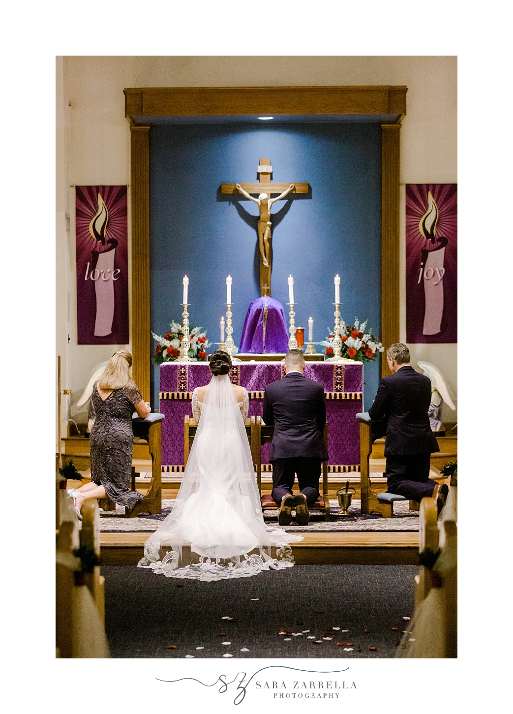 husband and wife kneel at alter with purple fabric during traditional Catholic ceremony in Rhode Island