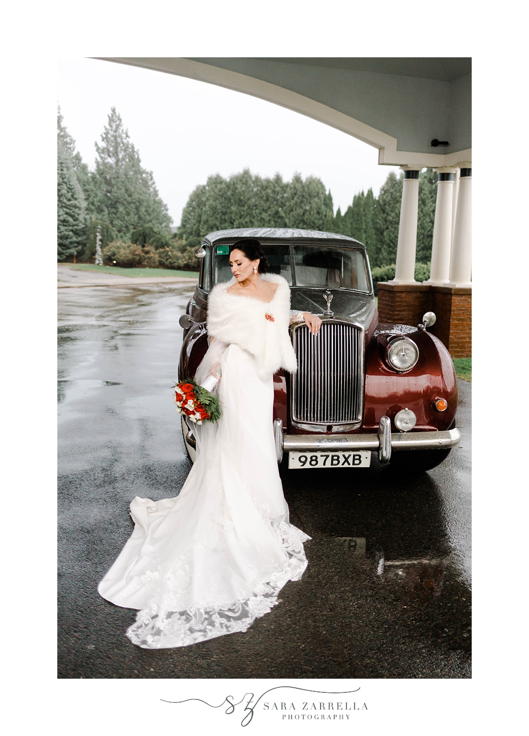 winter bride in gown with white wrap poses against cranberry classic car outside Quidnessett Country Club