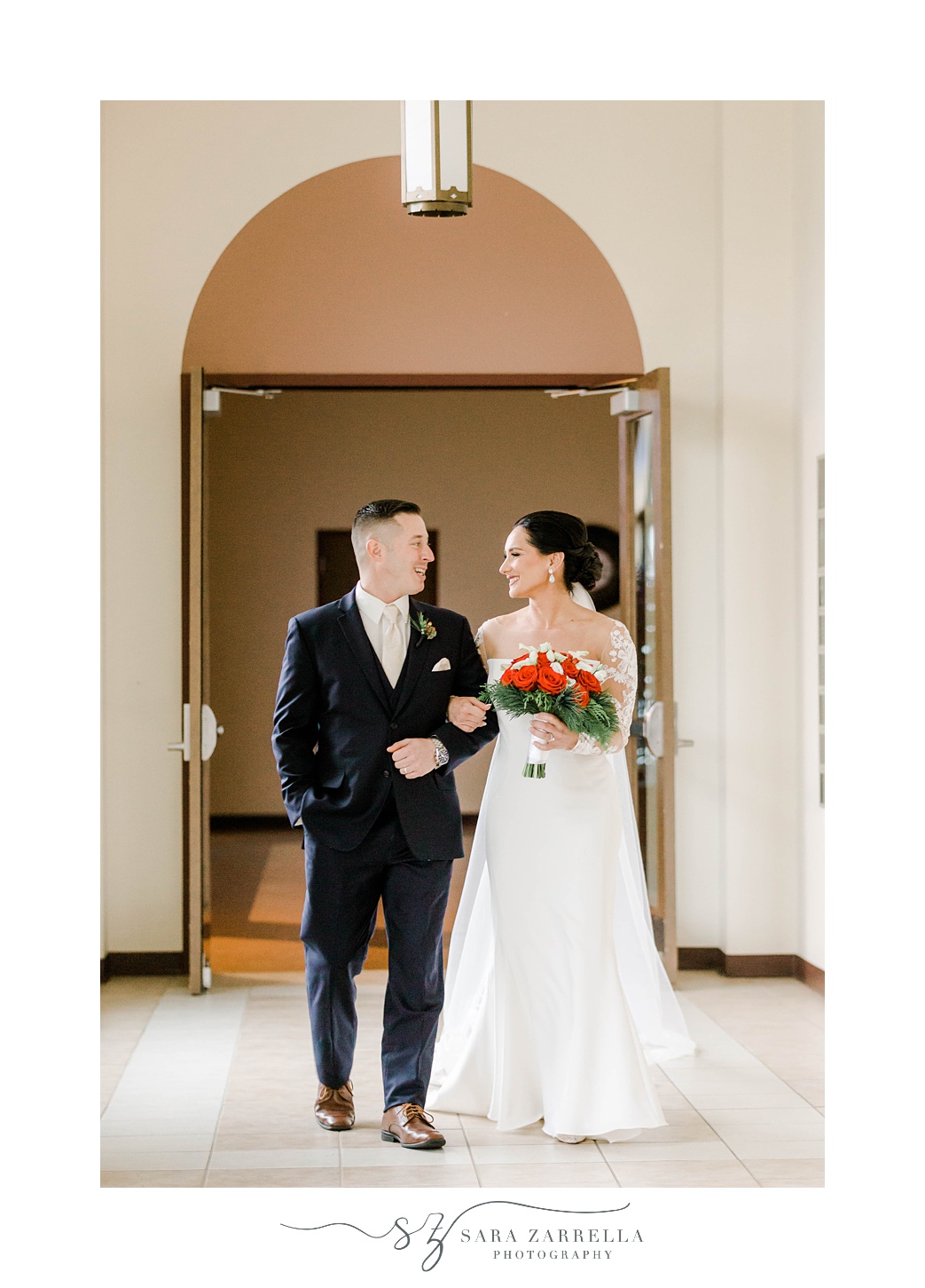bride and groom smile together walking through lobby of Quidnessett Country Club