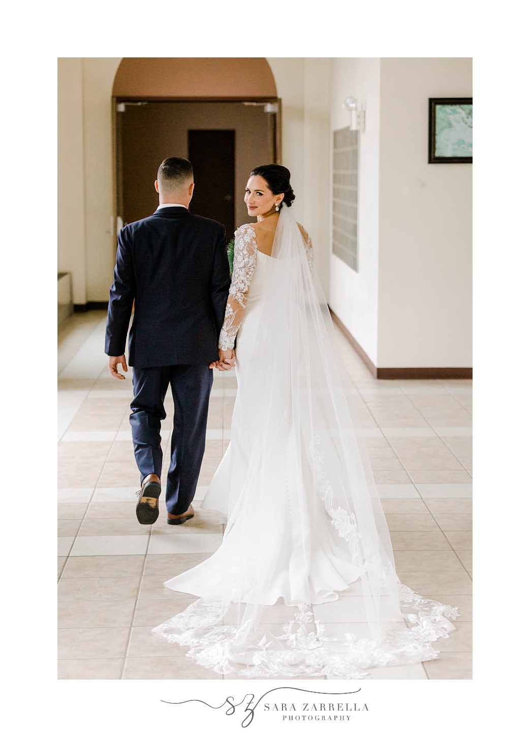groom holds bride's hand walking across lobby with her
