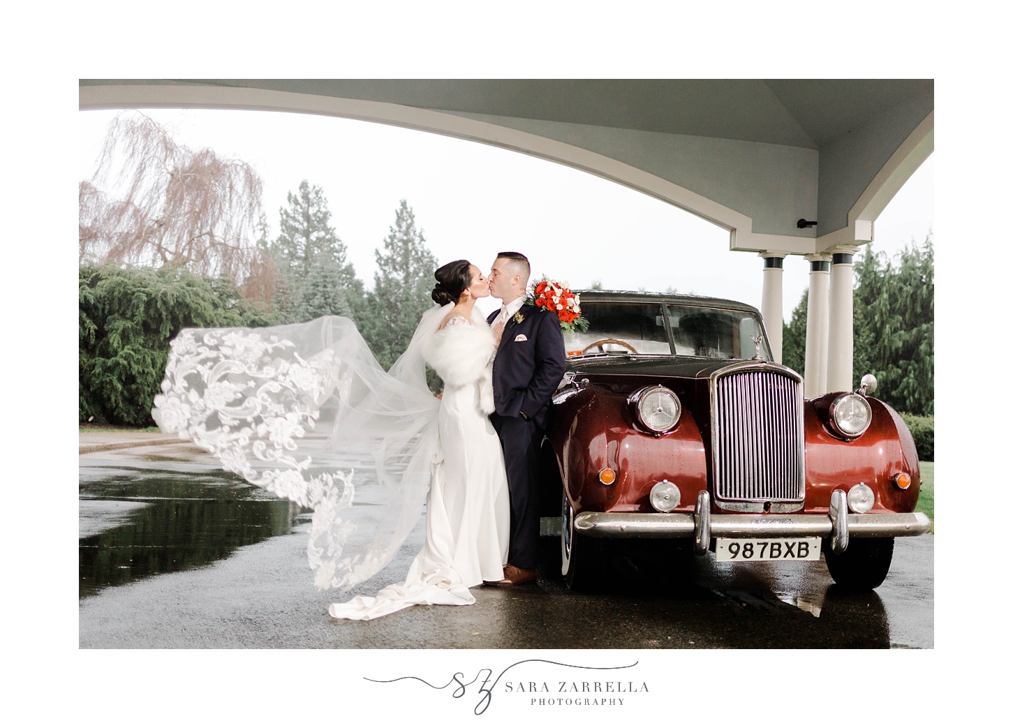 bride and groom hug next to 1937 Cranberry Rolls Royce Limo with bride's veil floating