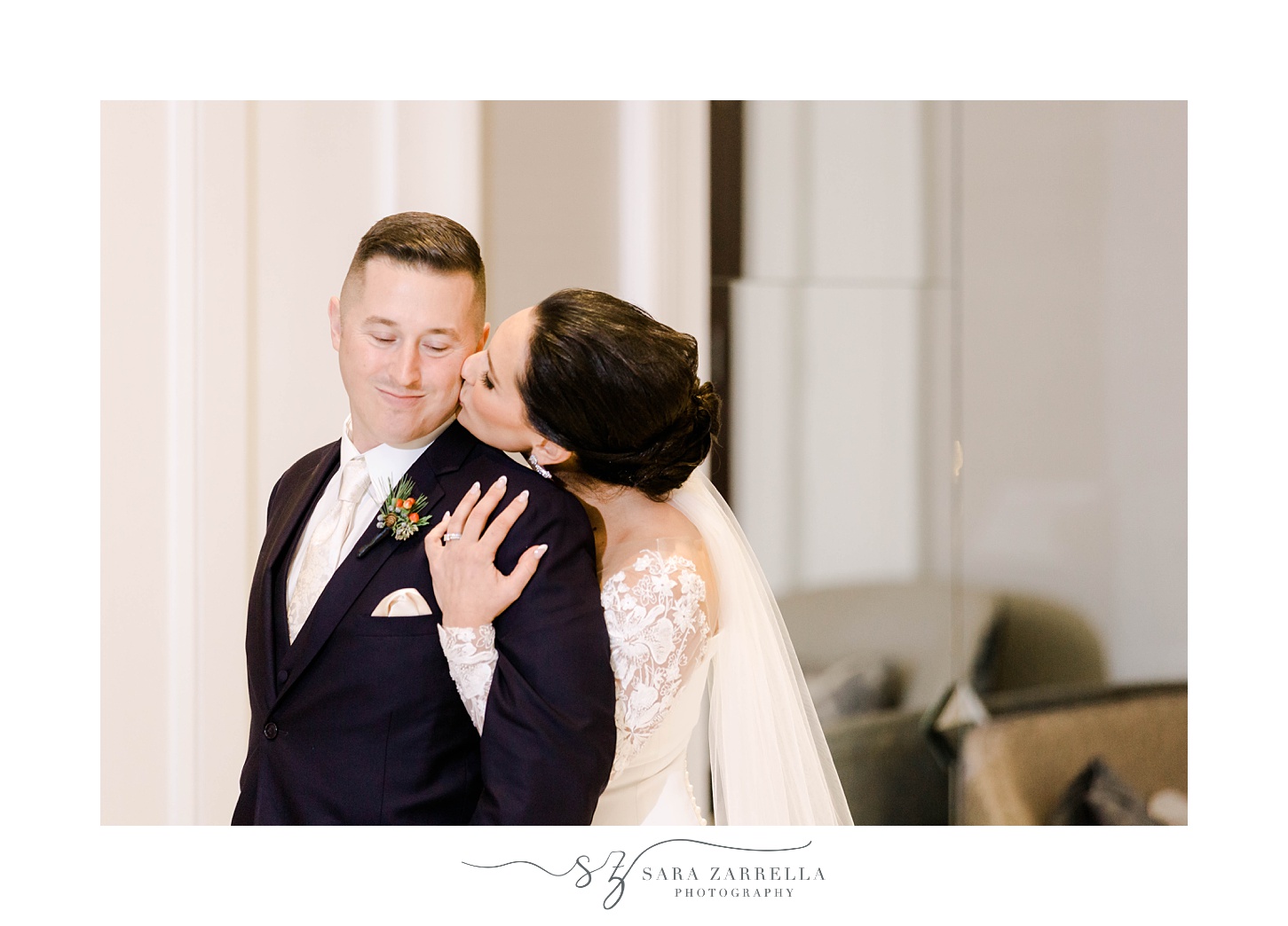bride in wedding gown with lace sleeves leans to kiss groom's cheek from behind him