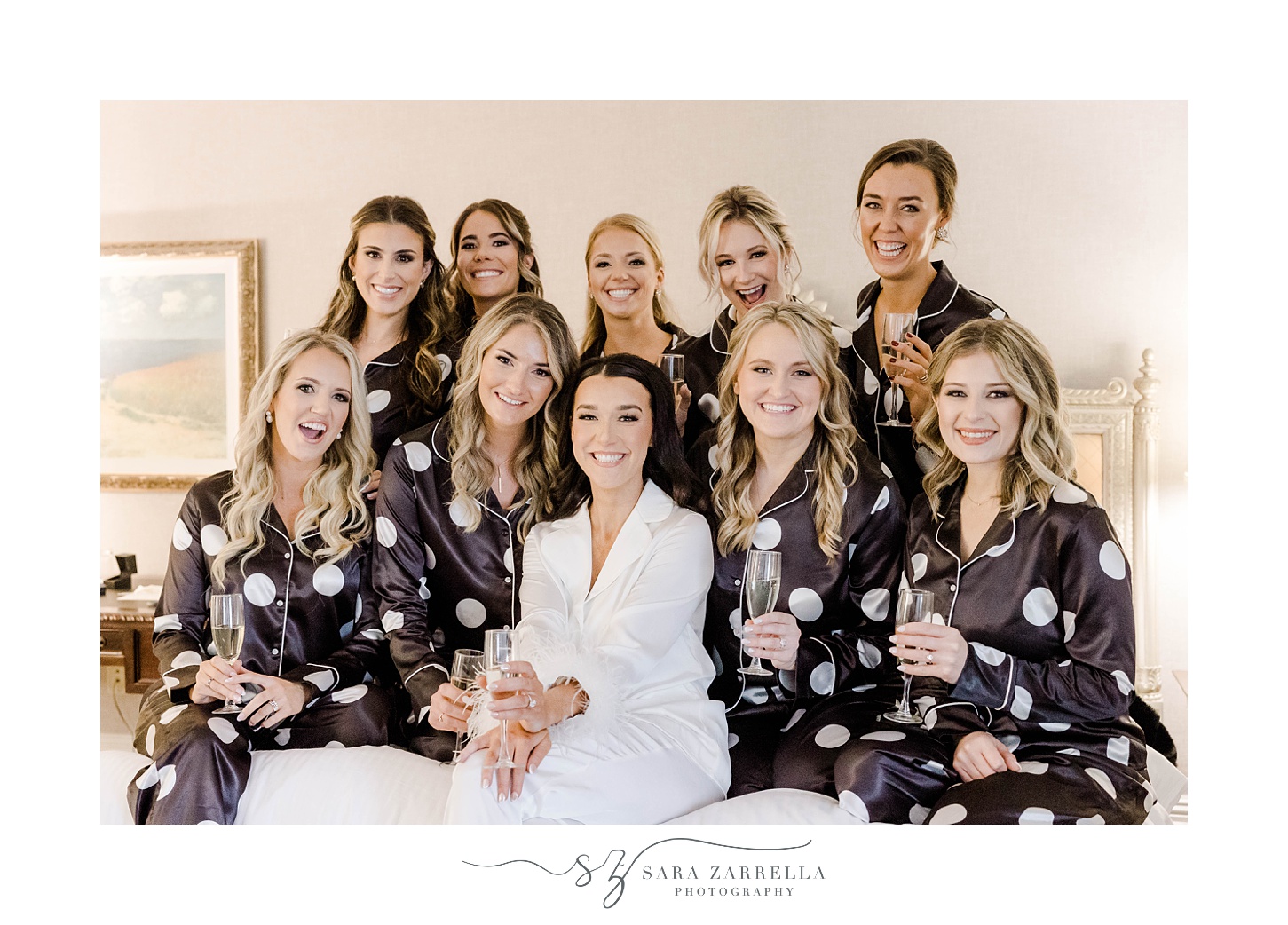 bride sits on bed at Belle Mer with bridesmaids in black robes 