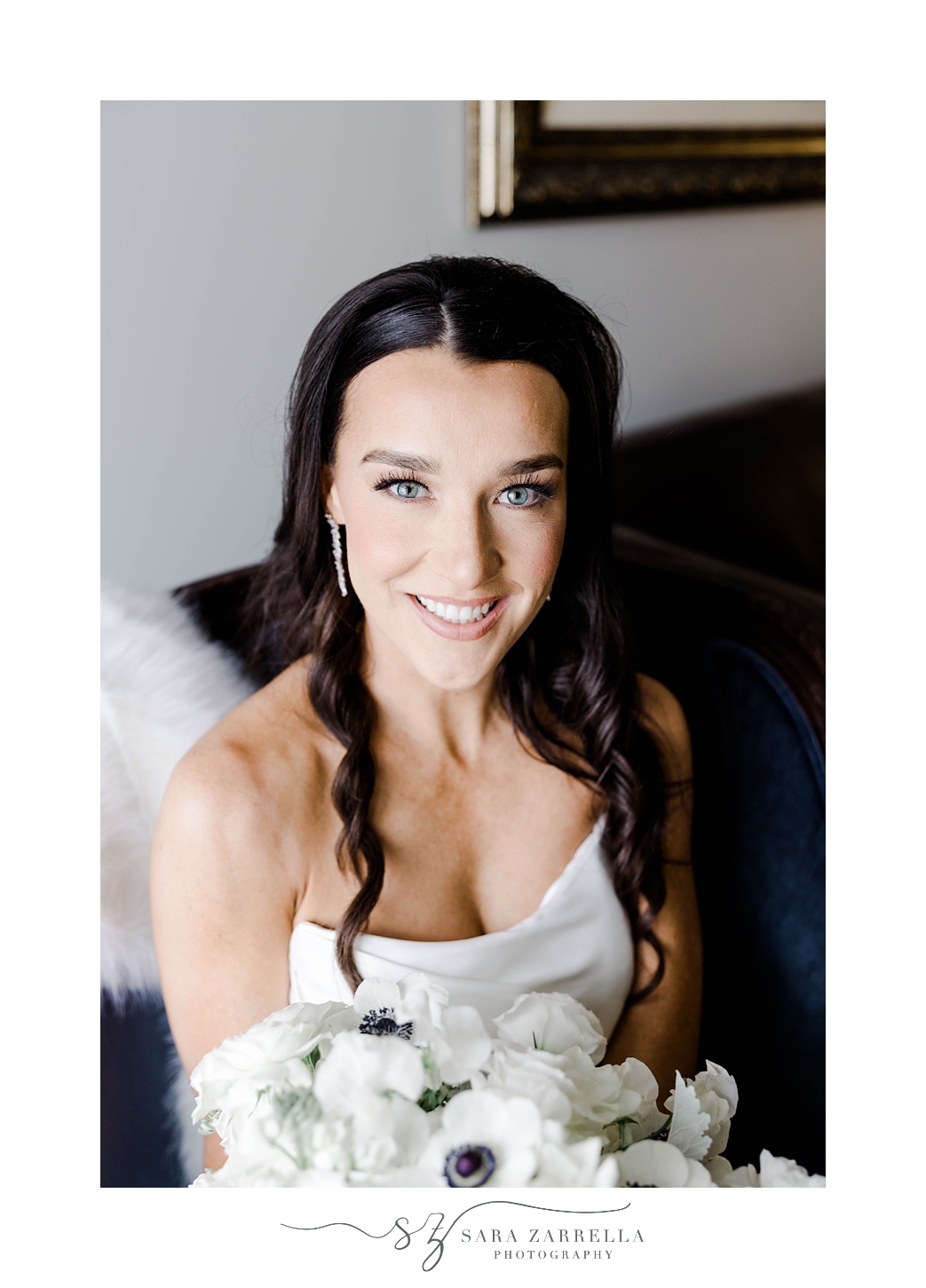 bride sits in strapless gown holding bouquet of anemones
