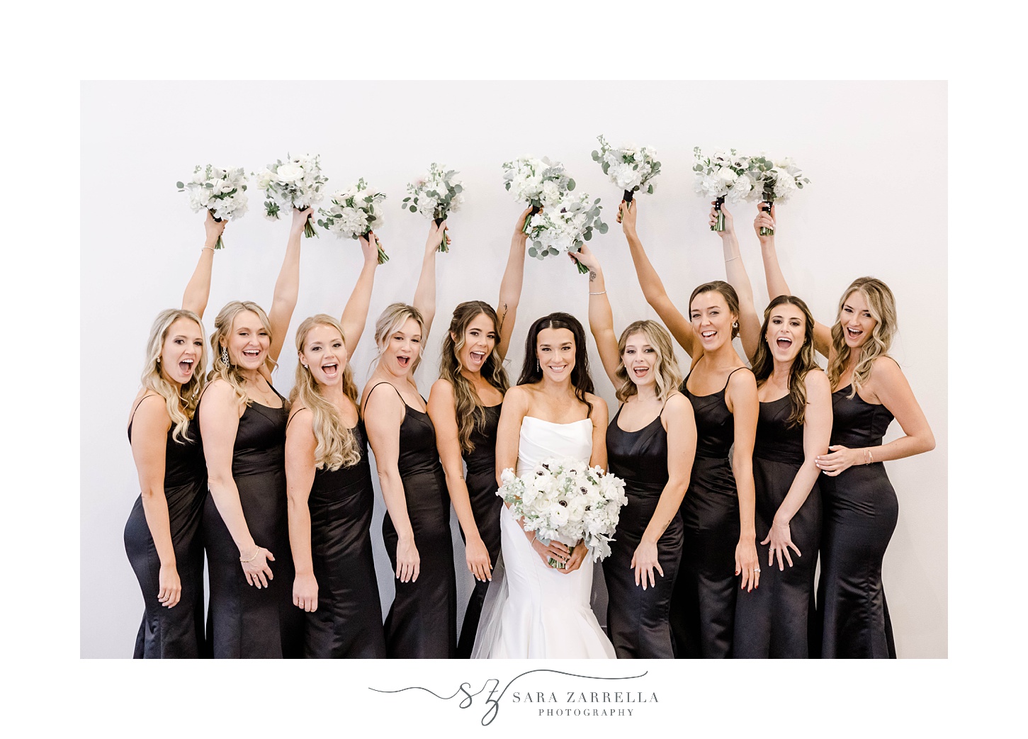 bride stands with bridesmaids in black gowns with bouquets of anemones