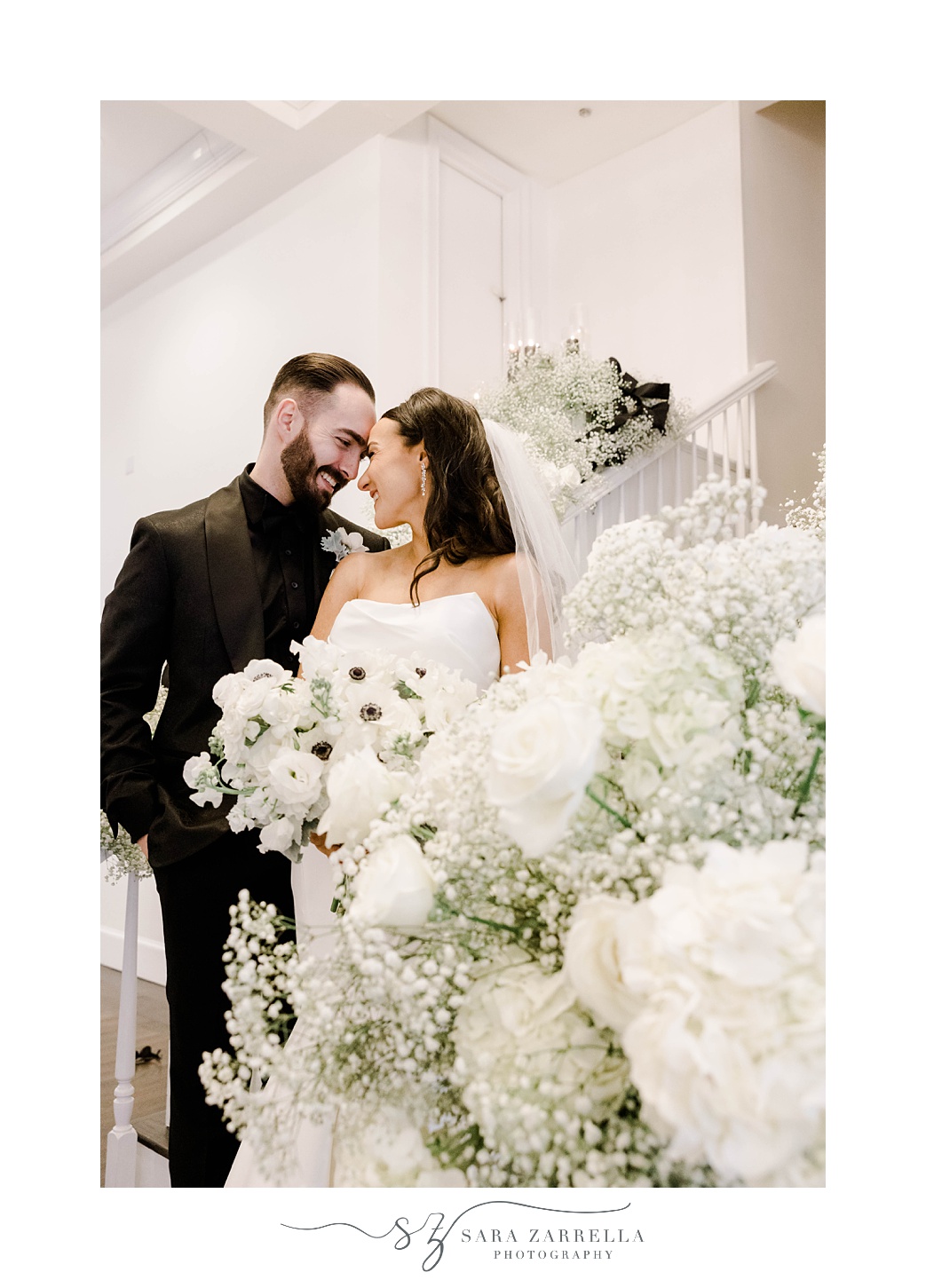 newlyweds hug behind white flowers on staircase at Belle Mer 