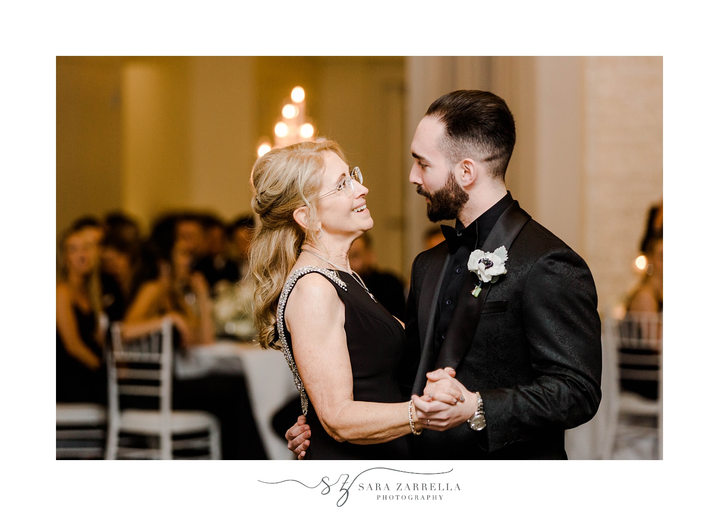 groom in all-black smiles at mother during dance at NYE wedding at Belle Mer
