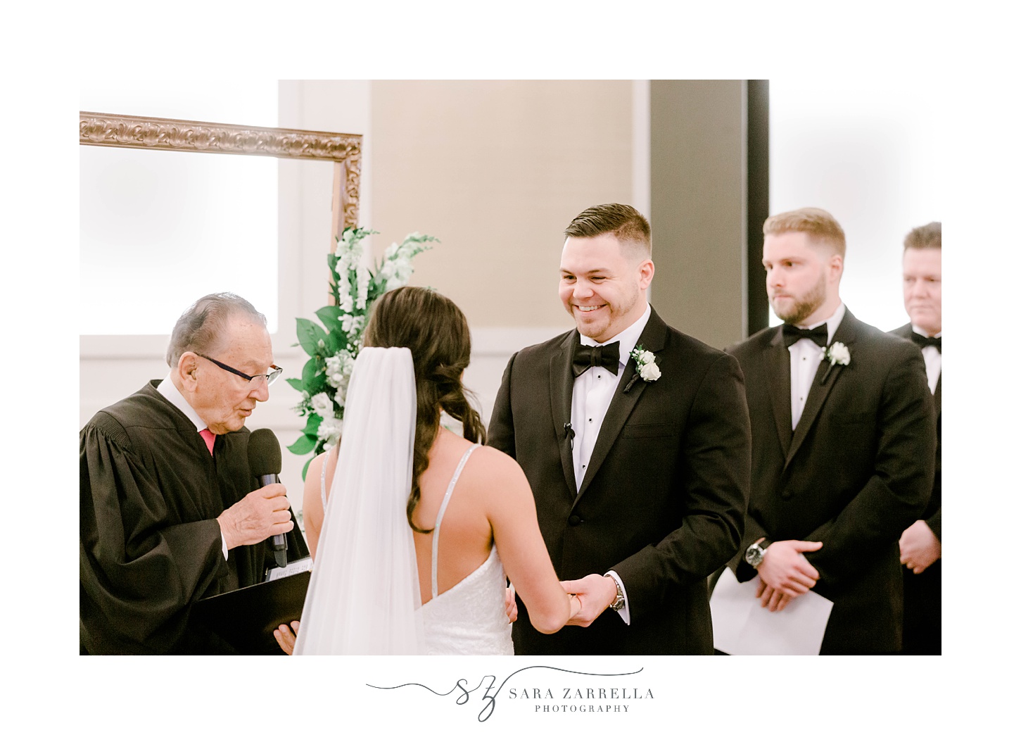 groom smiles at bride holding her hands during wedding ceremony in the atrium at the Crowne Plaza