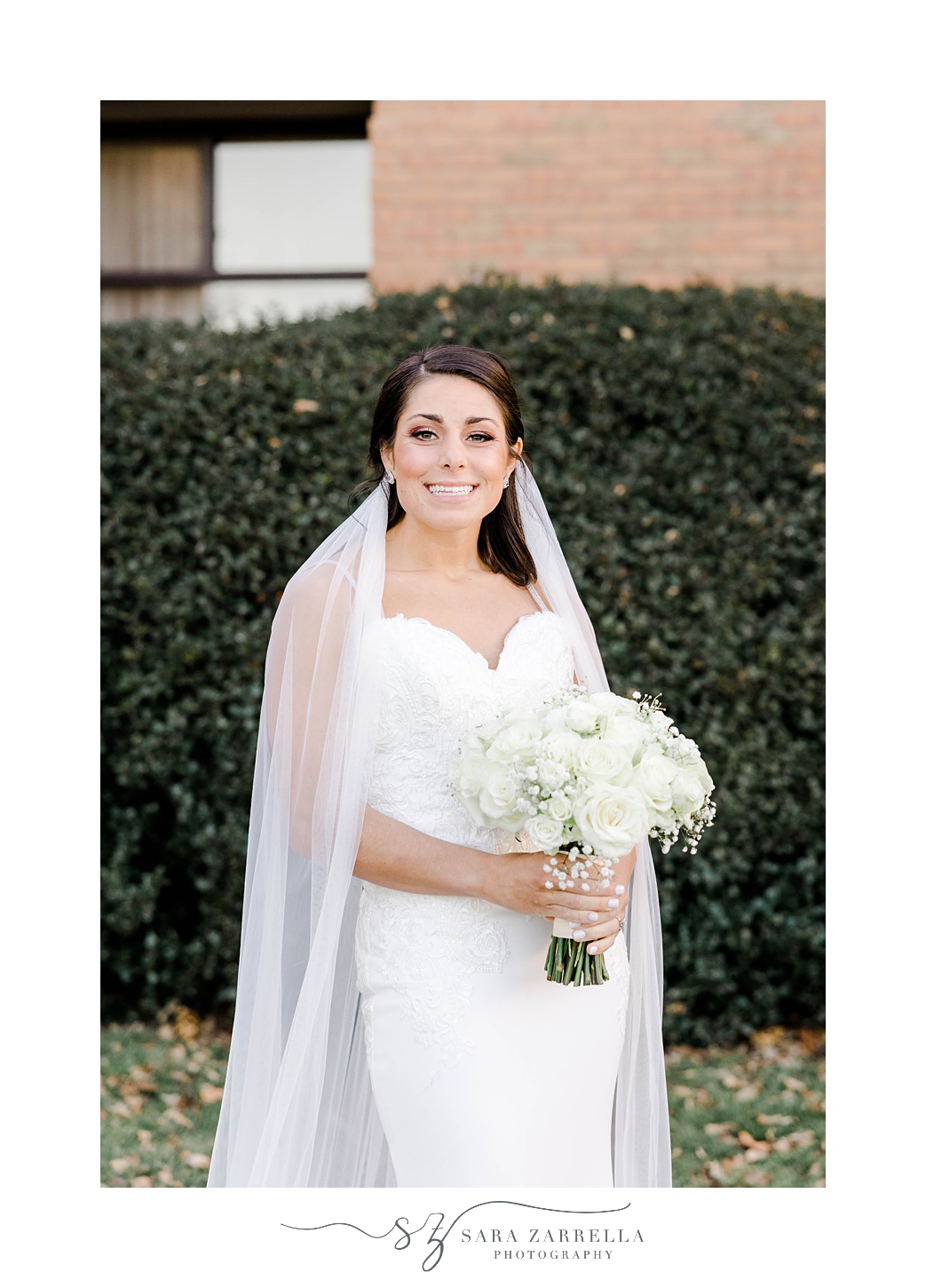 bride stands on lawn at the Crowne Plaza Warwick with veil around shoulders and all-white bouquet 