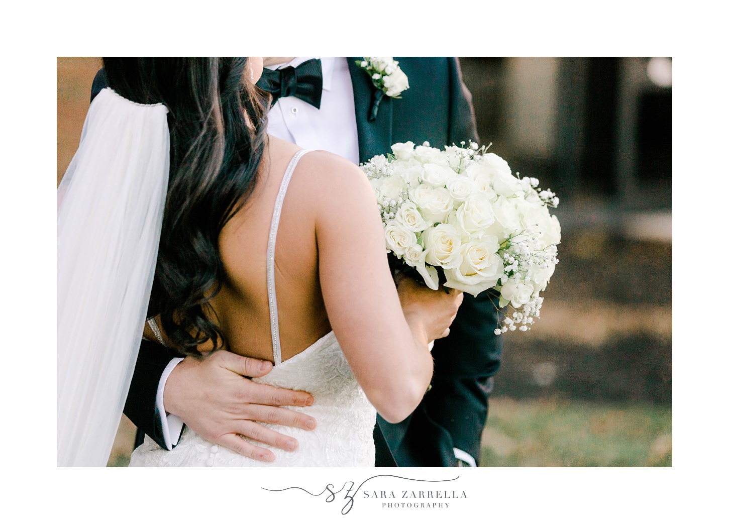 groom in black suit hugs bride to his hip holding bouquet of ivory roses 