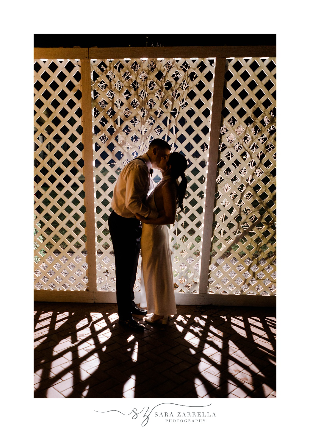 bride and groom kiss at night against white lattice fence