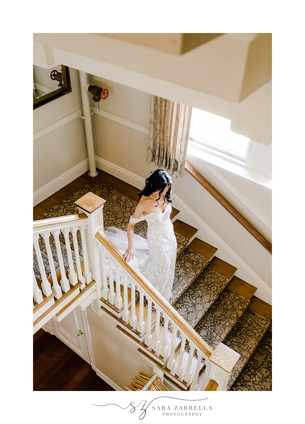 bride walks down staircase holding railing in off-the-shoulder wedding dress