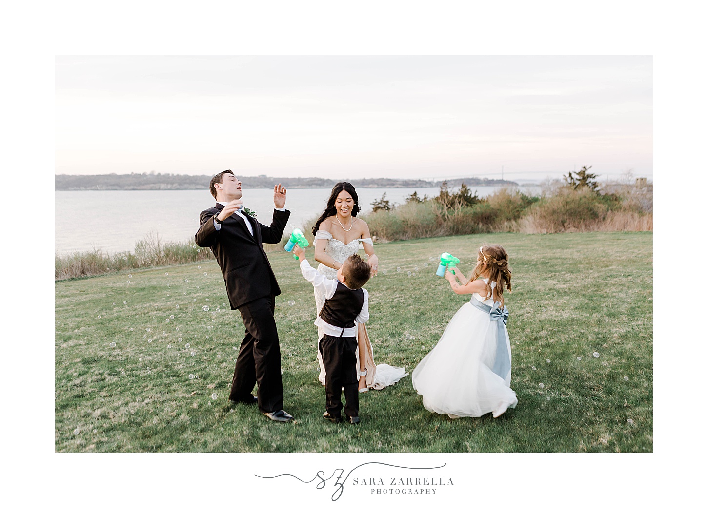 bride and groom laugh with flower girl and ring bearer blowing bubbles on them 