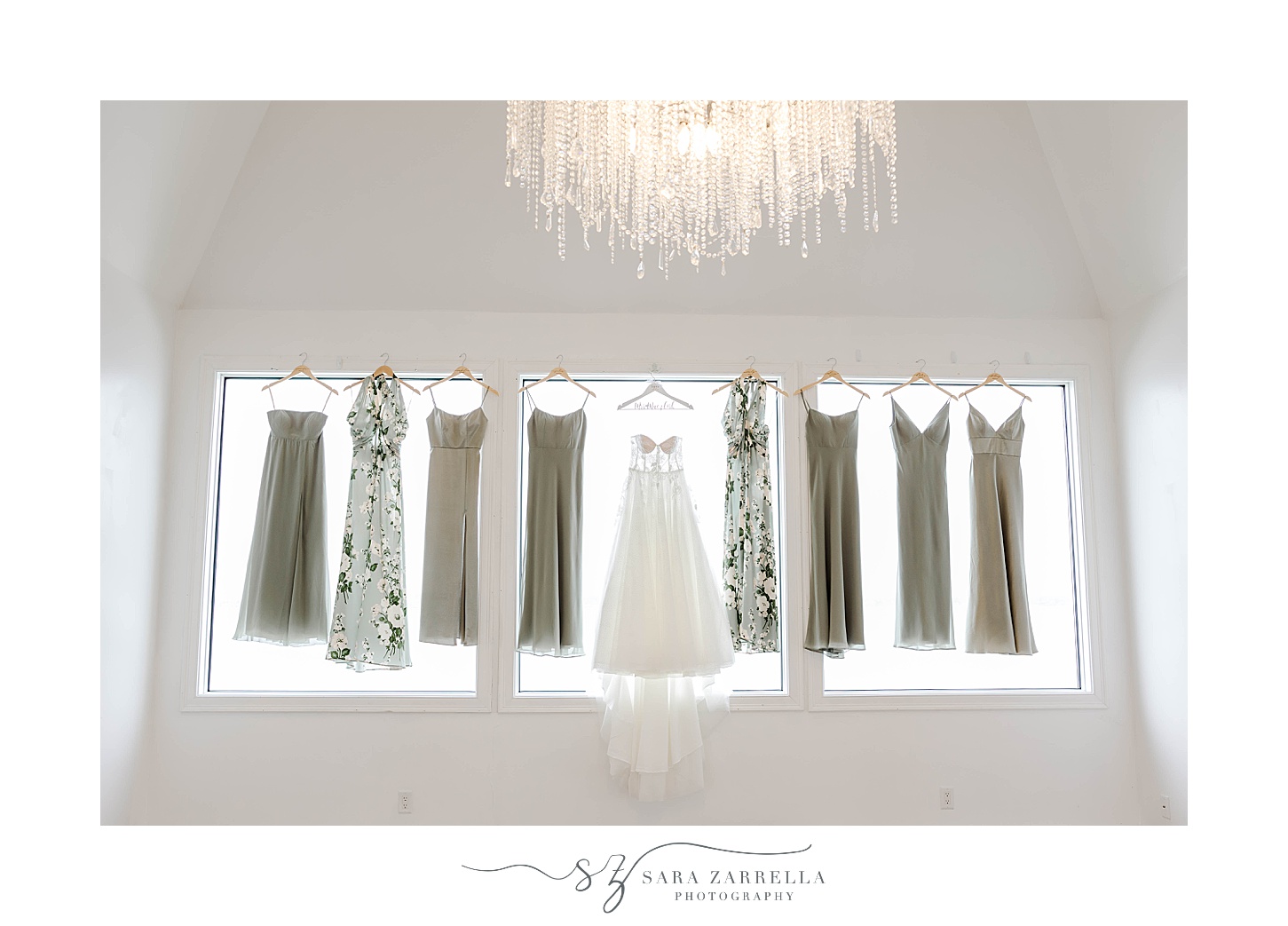 bride's dress hangs in window with bridesmaids gowns in mismatched shades of green