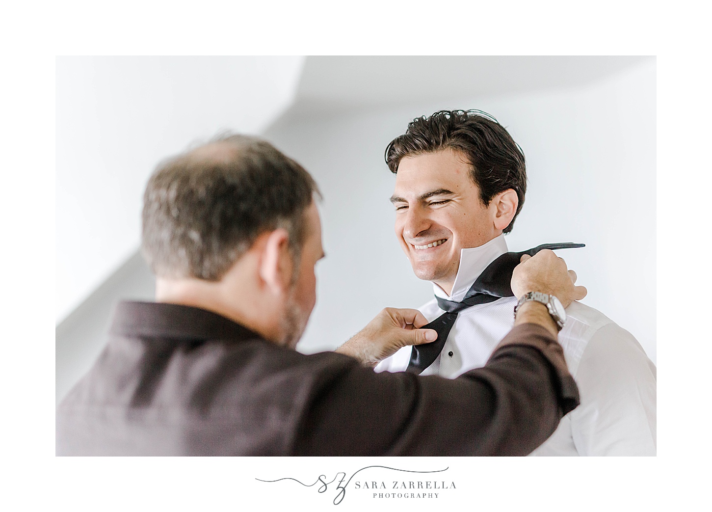 groom laughs with groomsman helping with bowtie