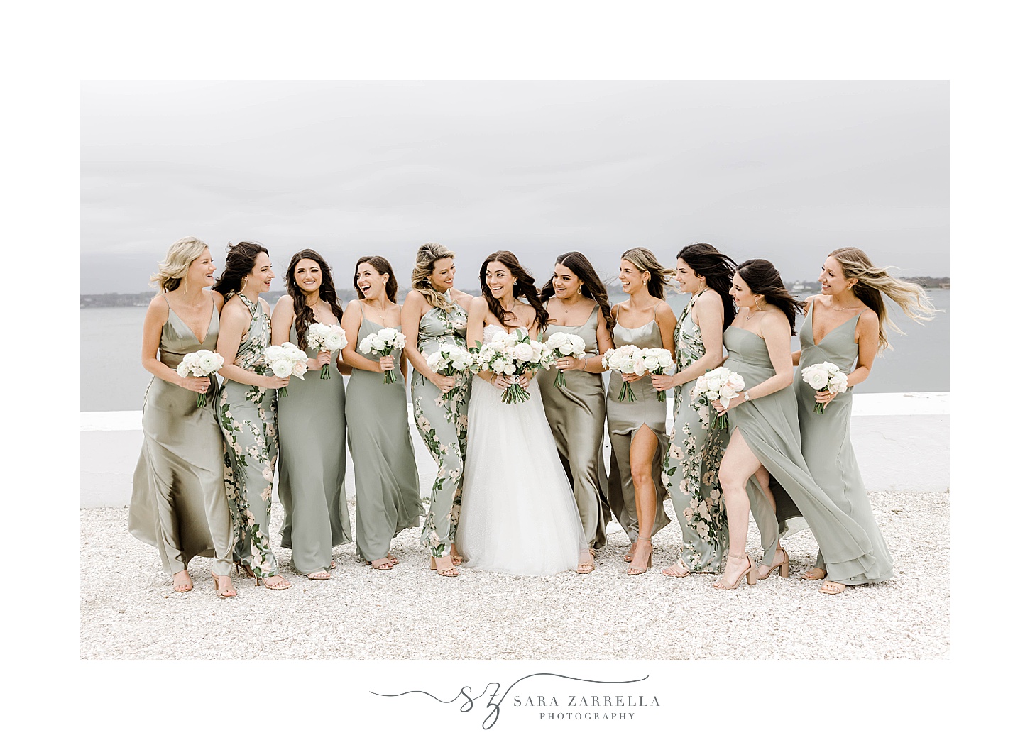 bride and bridesmaids in mismatched gowns huddle together on beach at Belle Mer Island House