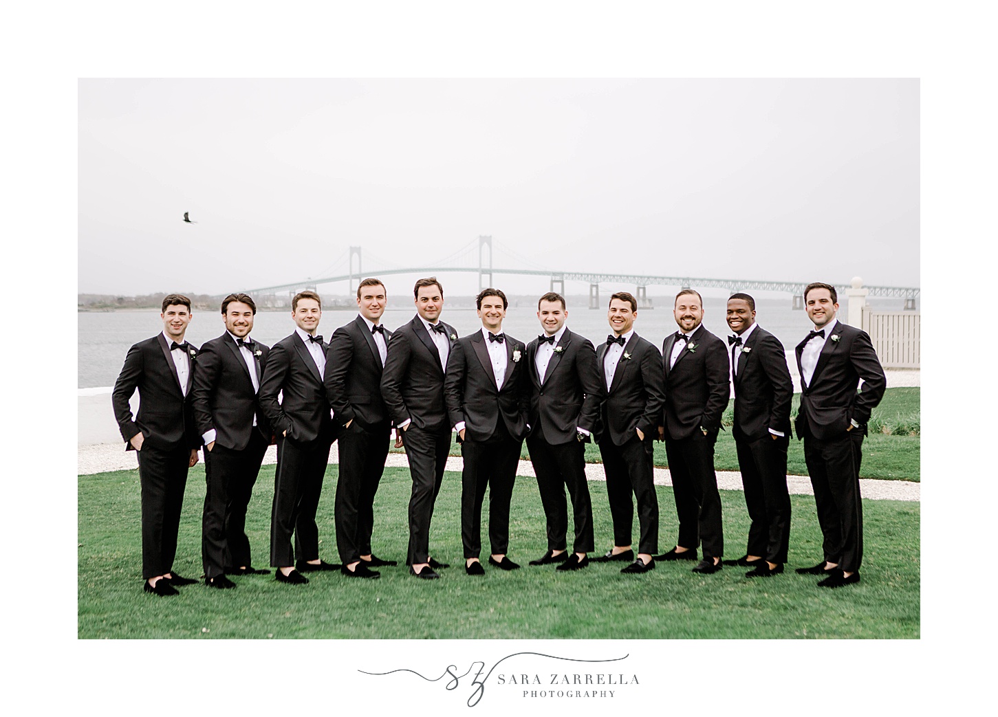groom and groomsmen pose in black suits near Newport Bridge at Belle Mer Island House