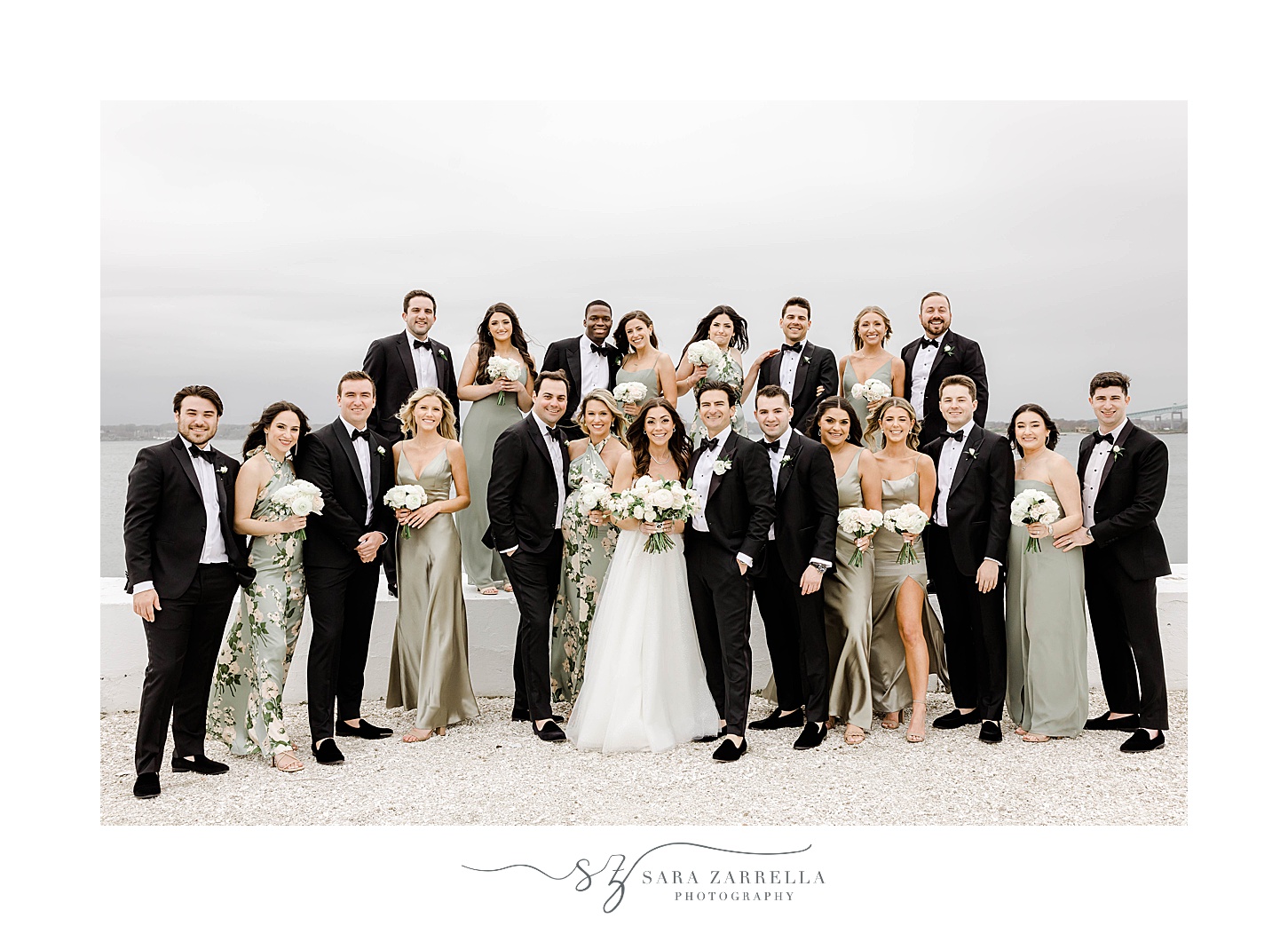 bride and groom stand with wedding party in black suits and green dresses 