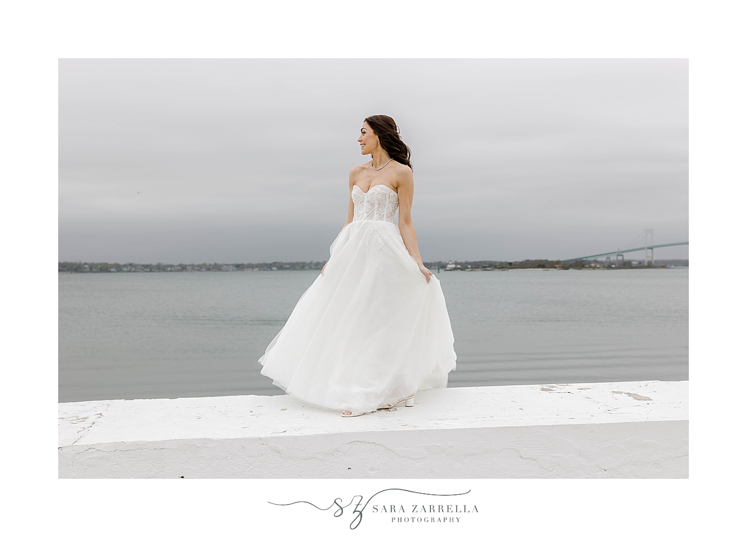 bride stands on white wall looking at Narragansett Bay