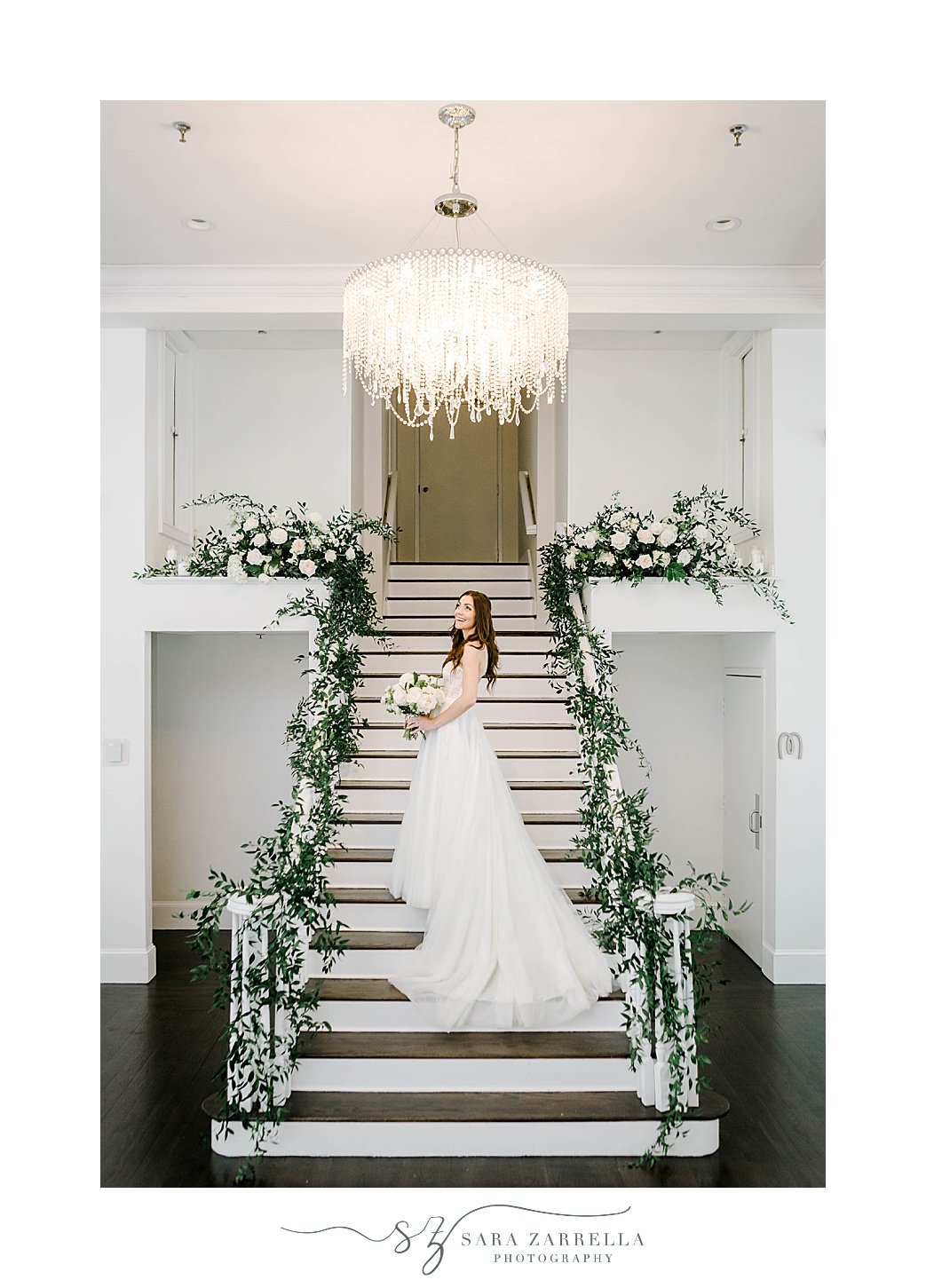 bride stands on staircase with florals down railing at Belle Mer Island House