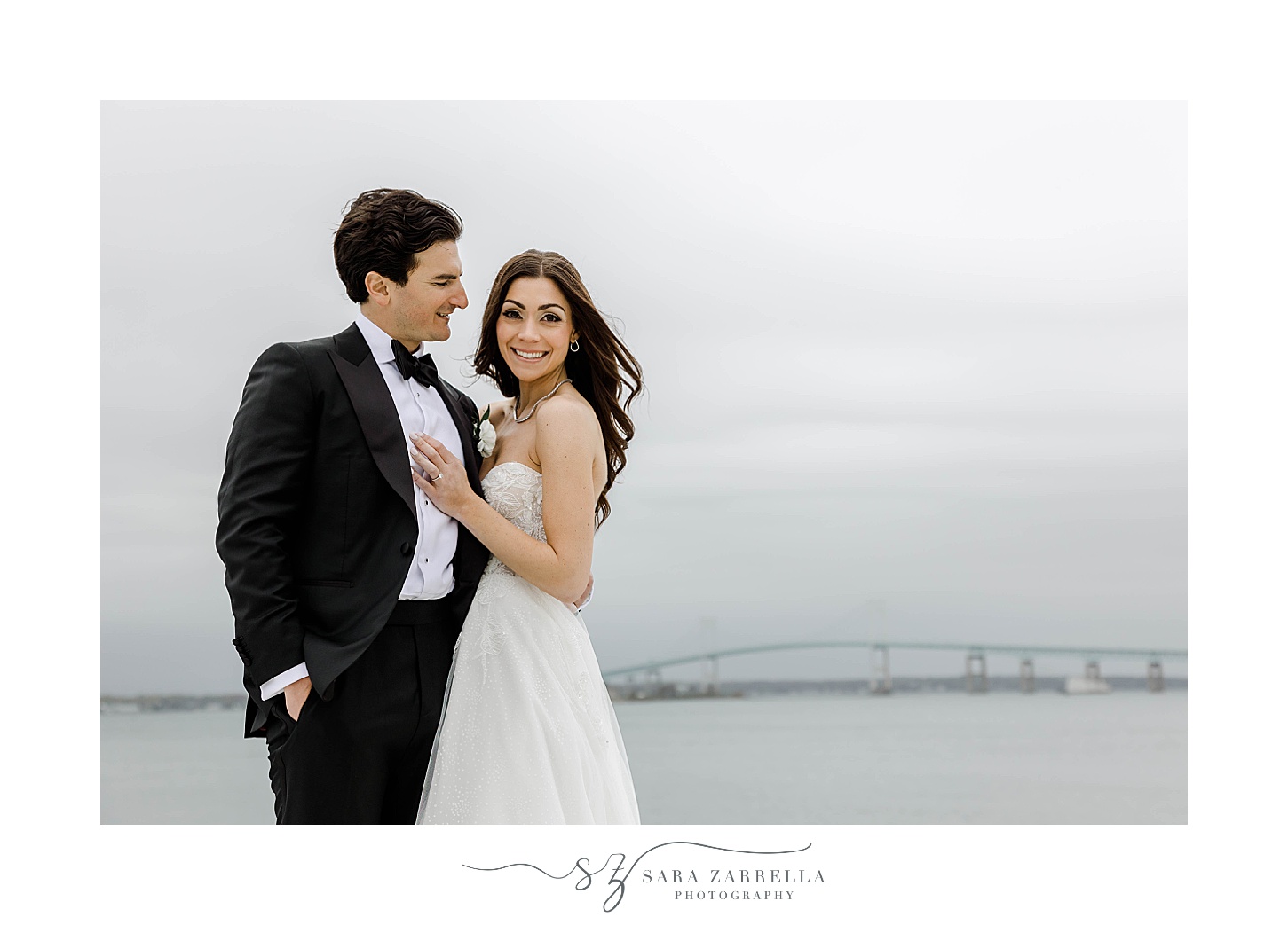 groom hugs bride to him looking at her in front of Narragansett Bay 
