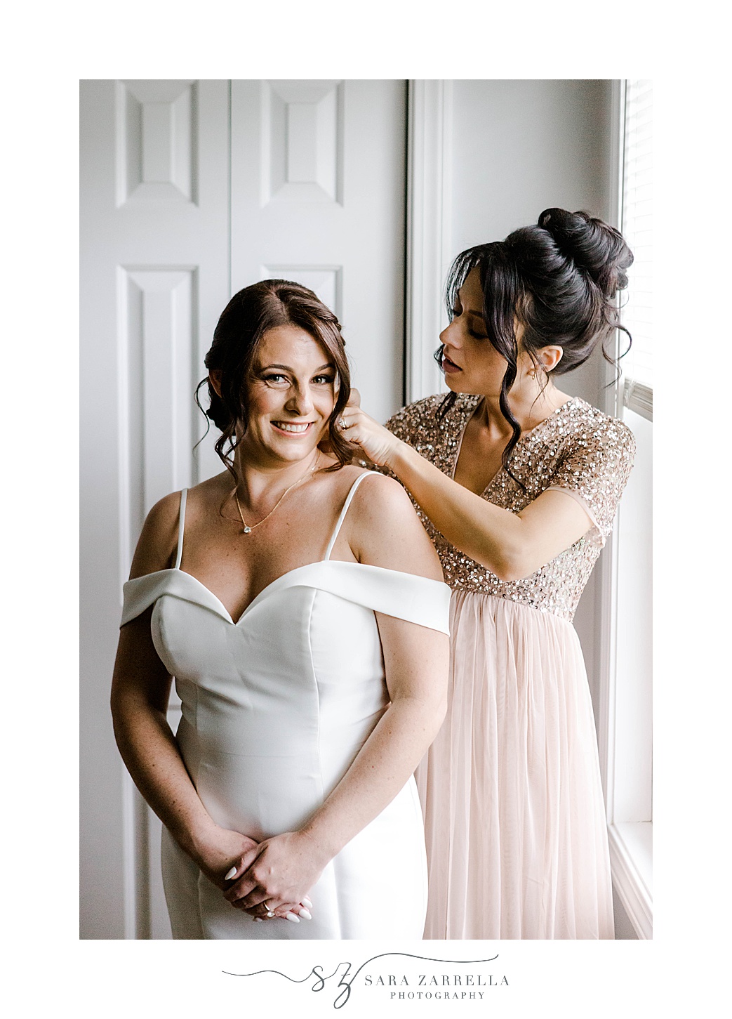 mother in peach dress helps bride with necklace and wedding dress