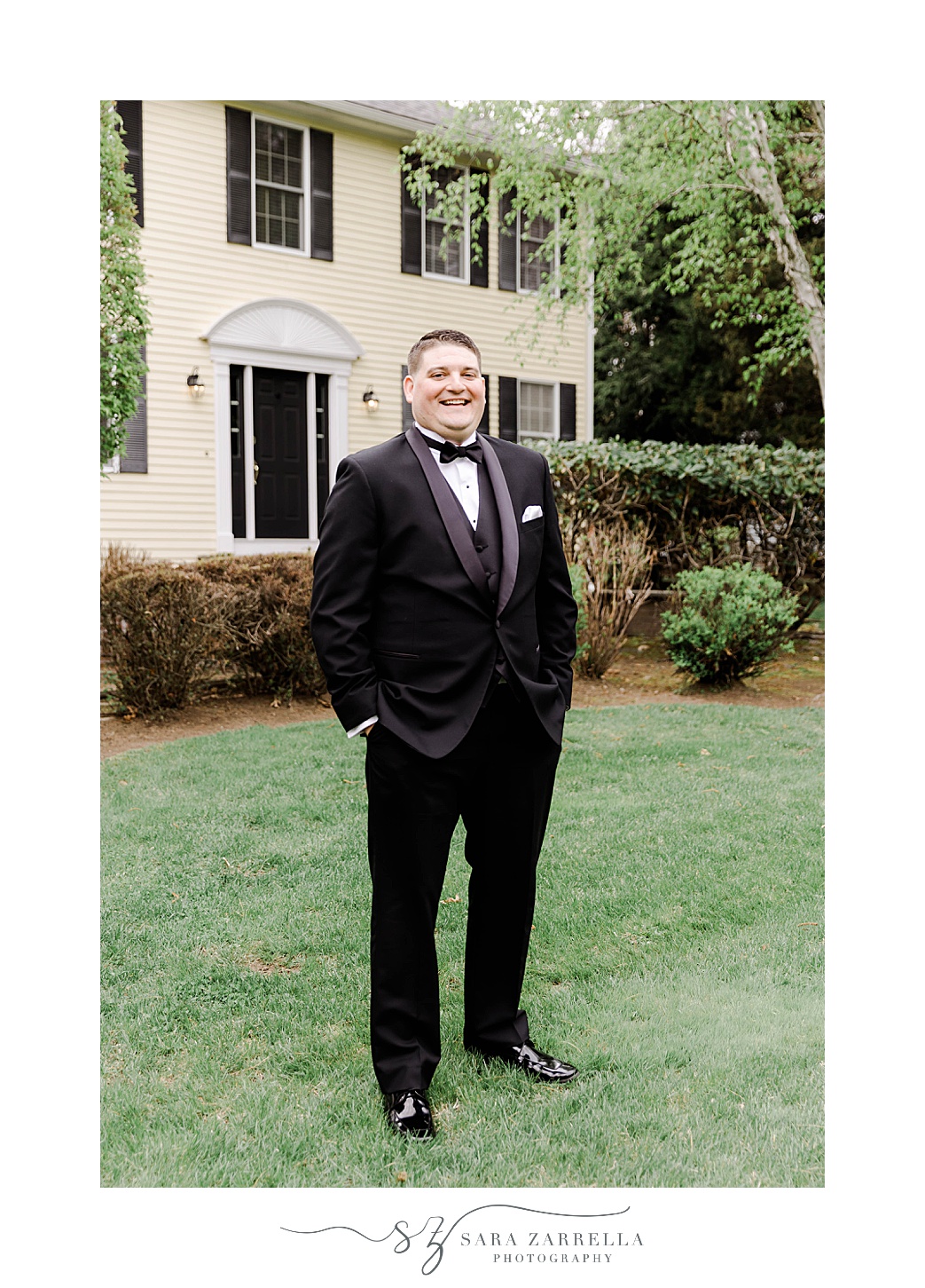 groom stands in black tux on front lawn in Rhode Island