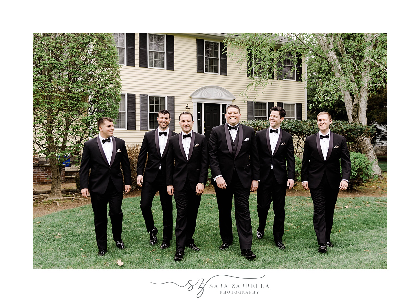 groom walks with groomsmen on lawn in classic black suits