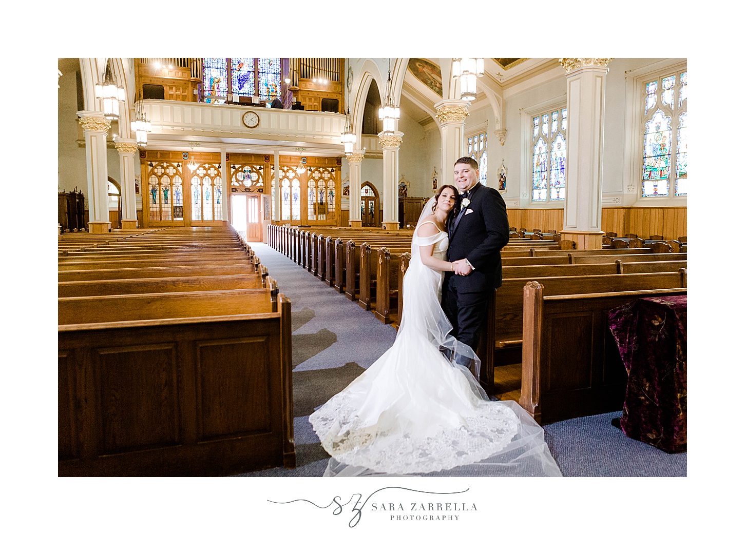 newlyweds pose between seats in chapel at Our Lady of the Rosary