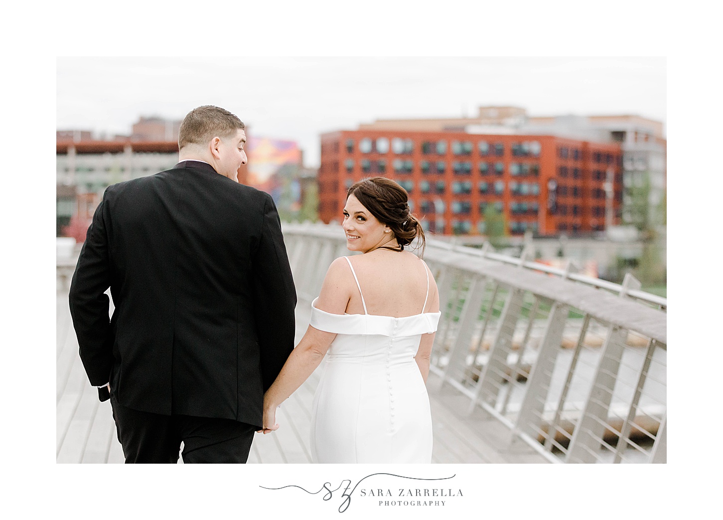 bride and groom hold hands walking across Providence Pedestrian Bridge